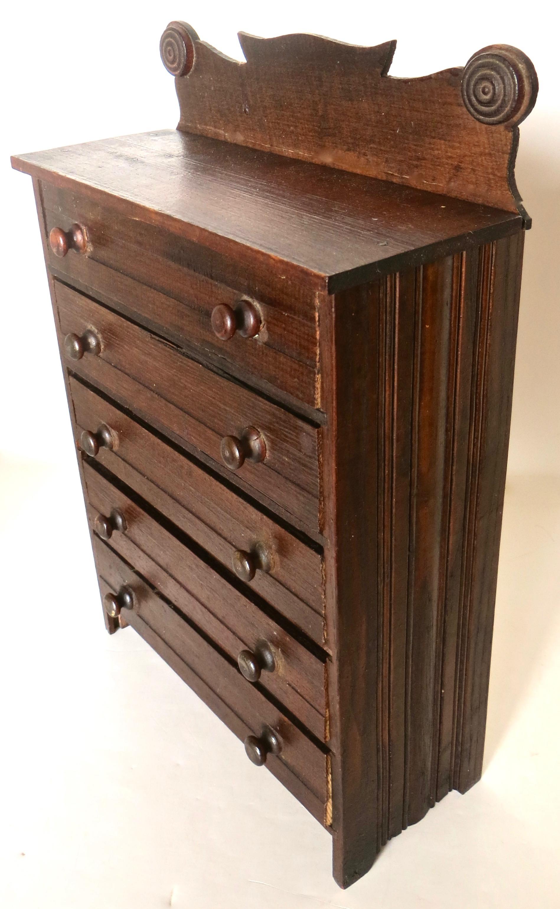 This late 19th century miniature 5-drawer dresser was likely used as a salesman sample by an itinerant sales person who traveled the countryside promoting his articles, usually by seeking out merchants to take orders based on this miniature chest,