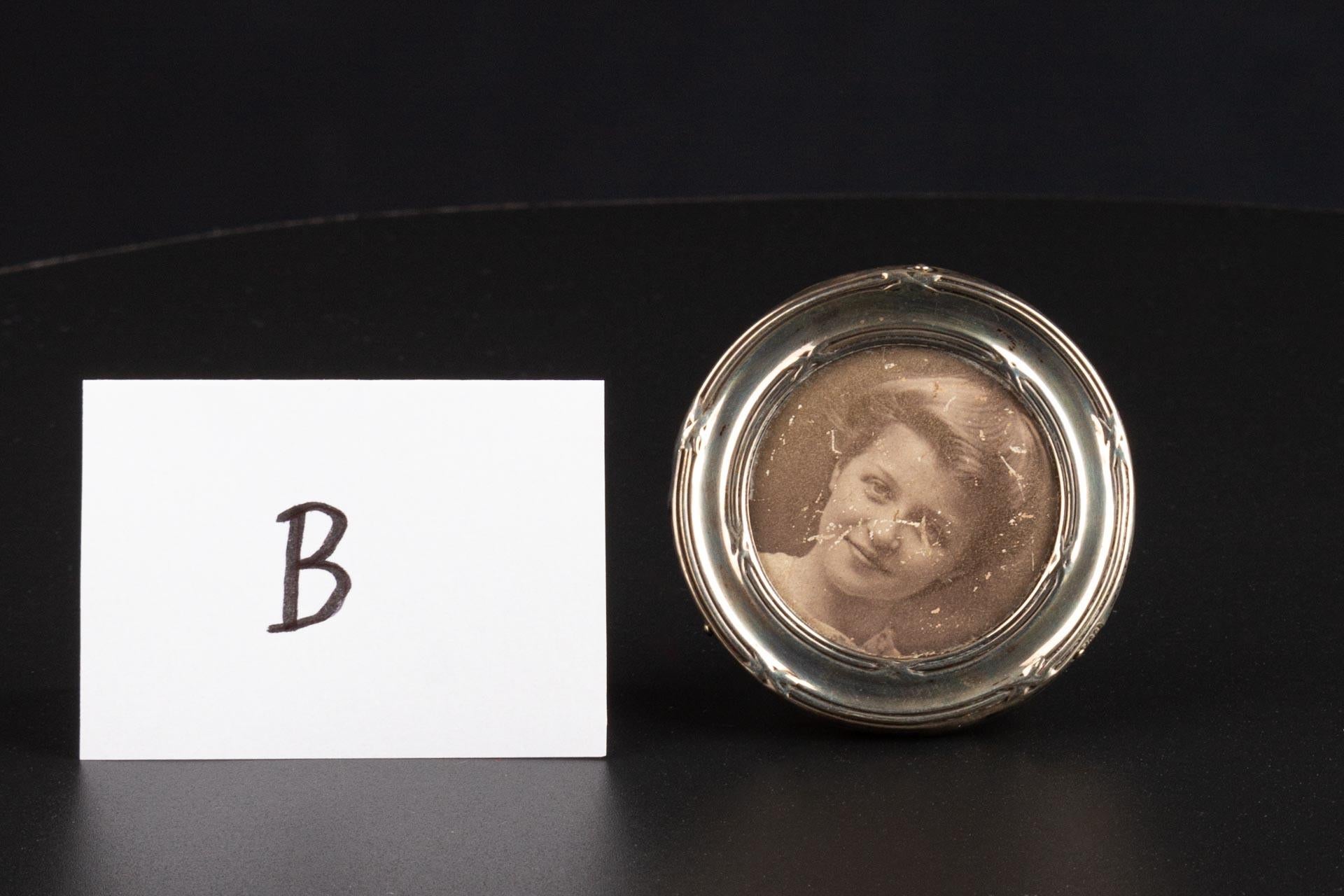 Durchmesser insgesamt 5 cm, Durchmesser Foto 3,5 cm.

Runder, aufstellbarer Bilderrahmen in Silber. Entsprechende Briefmarken befinden sich am Rand des Rahmens, Sie können sie auf den Fotos sehen. 
Der Ständer auf der Rückseite ist aus Leder