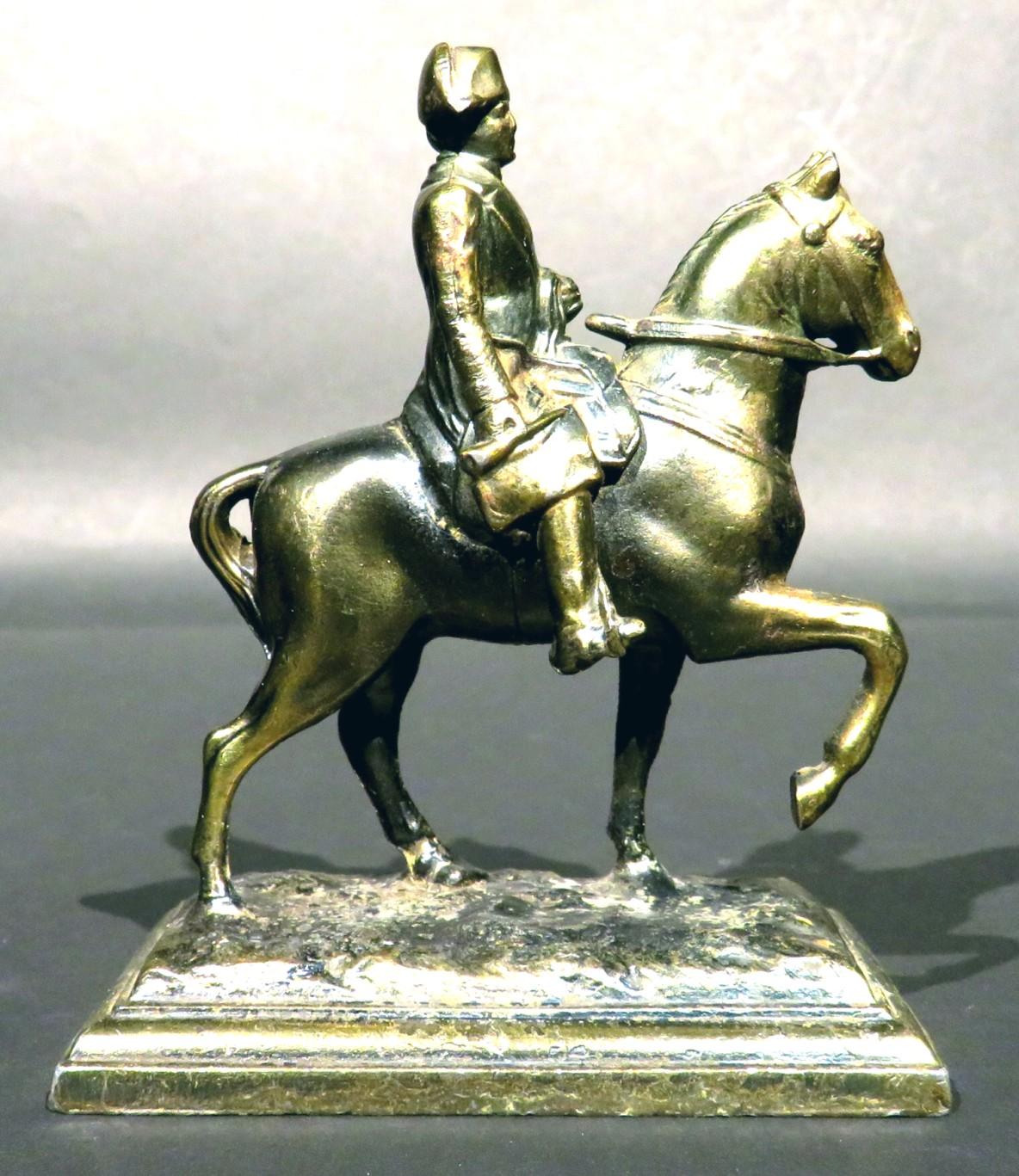 An early 20th century gilt patinated spelter figure of Napoleon Bonaparte on horseback, dressed in military attire and tri-corn hat, mounted atop a naturalistically modelled rocky ground.         (Apparently having been previously mounted on top of