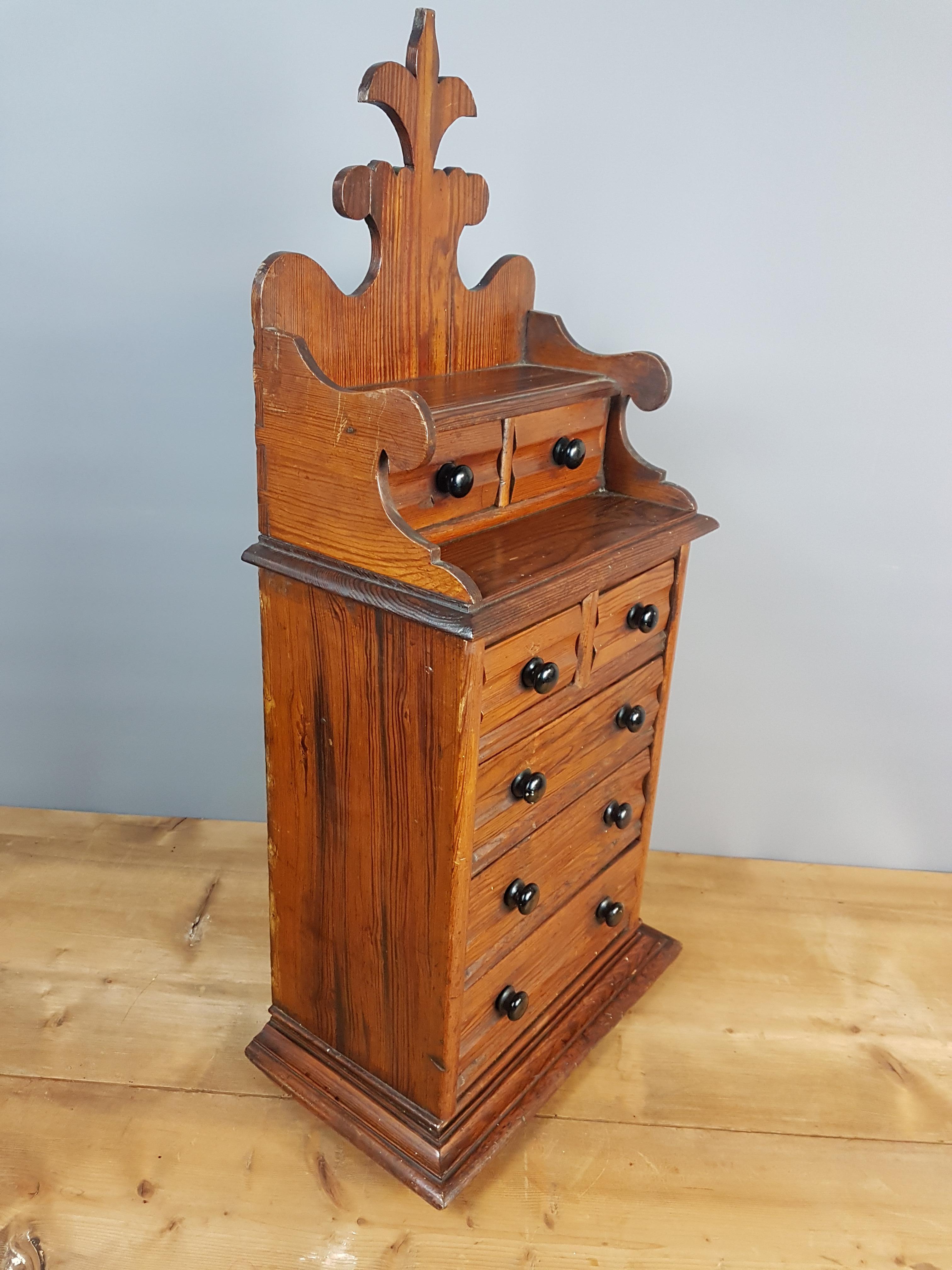 A very sweet and decorative pitch pine miniature apprentice chest of drawers with decorative scrolled upstand. The chest is very well made with even the to section being dovetailed into the bottom on the back, there are marks, dents, a few scratches