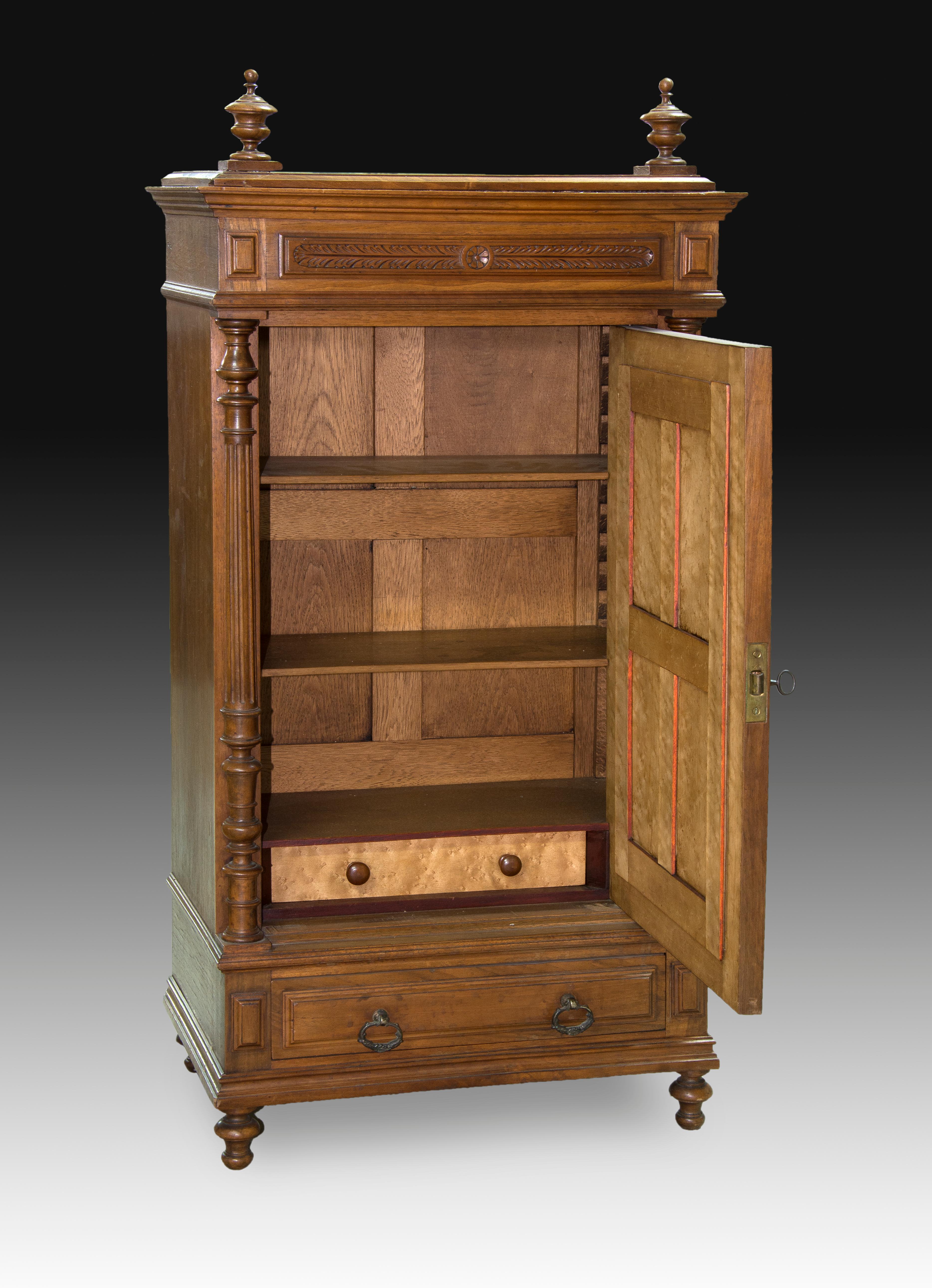 Miniature moon wardrobe. Walnut wood. XIX century. 
Miniature wardrobe with a door (inside, two shelvesand a drawer) and a drawer with two handles, whichhas a mirror on the outside and a decoration based onarchitectural elements, plants and