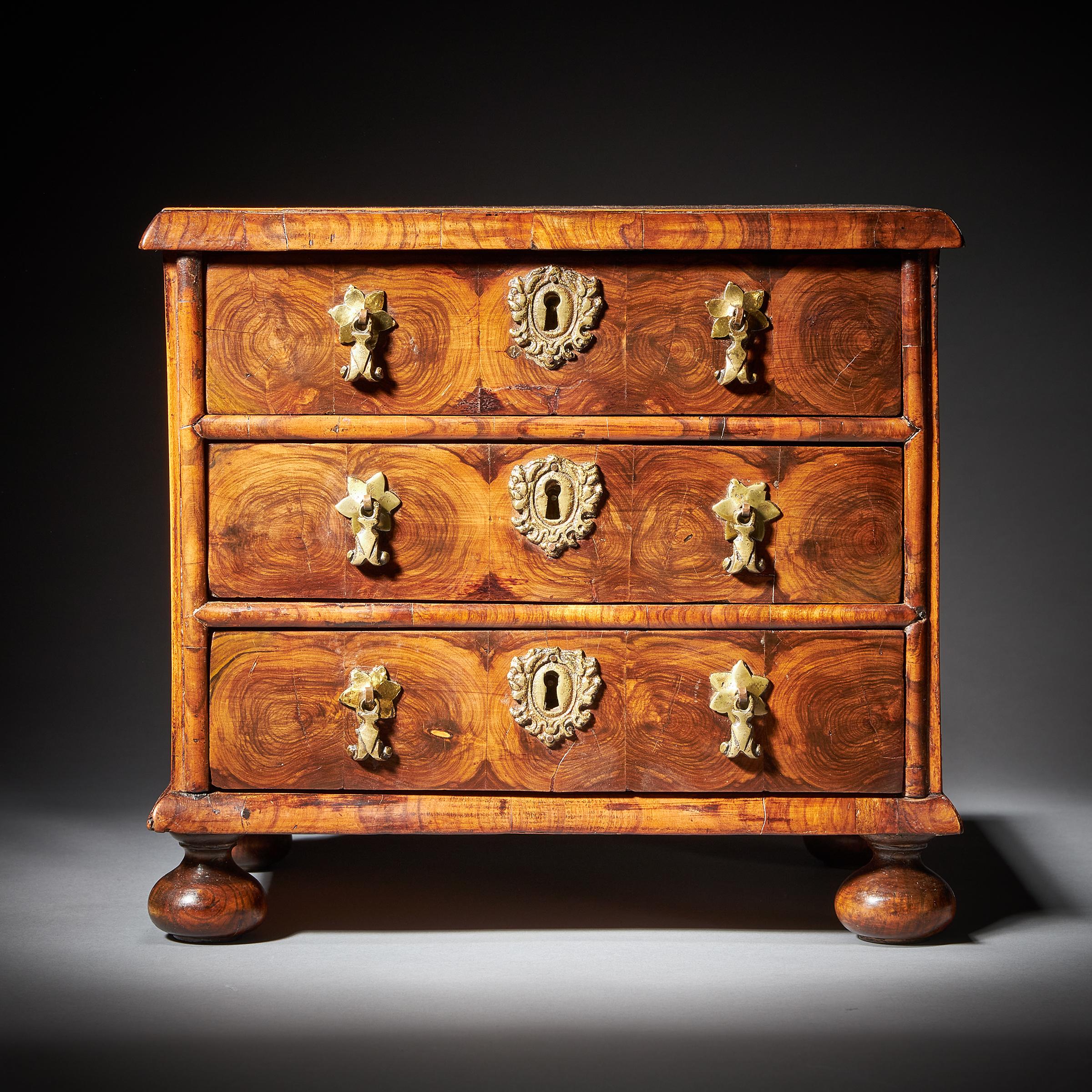From the reign of King William & Queen Mary (1688-1702), England.

The finely holly-banded and cross-grain moulded top is beautifully veneered in roundels of hand-cut olive oysters and lined in boxwood stringing in a geometric form. Over three