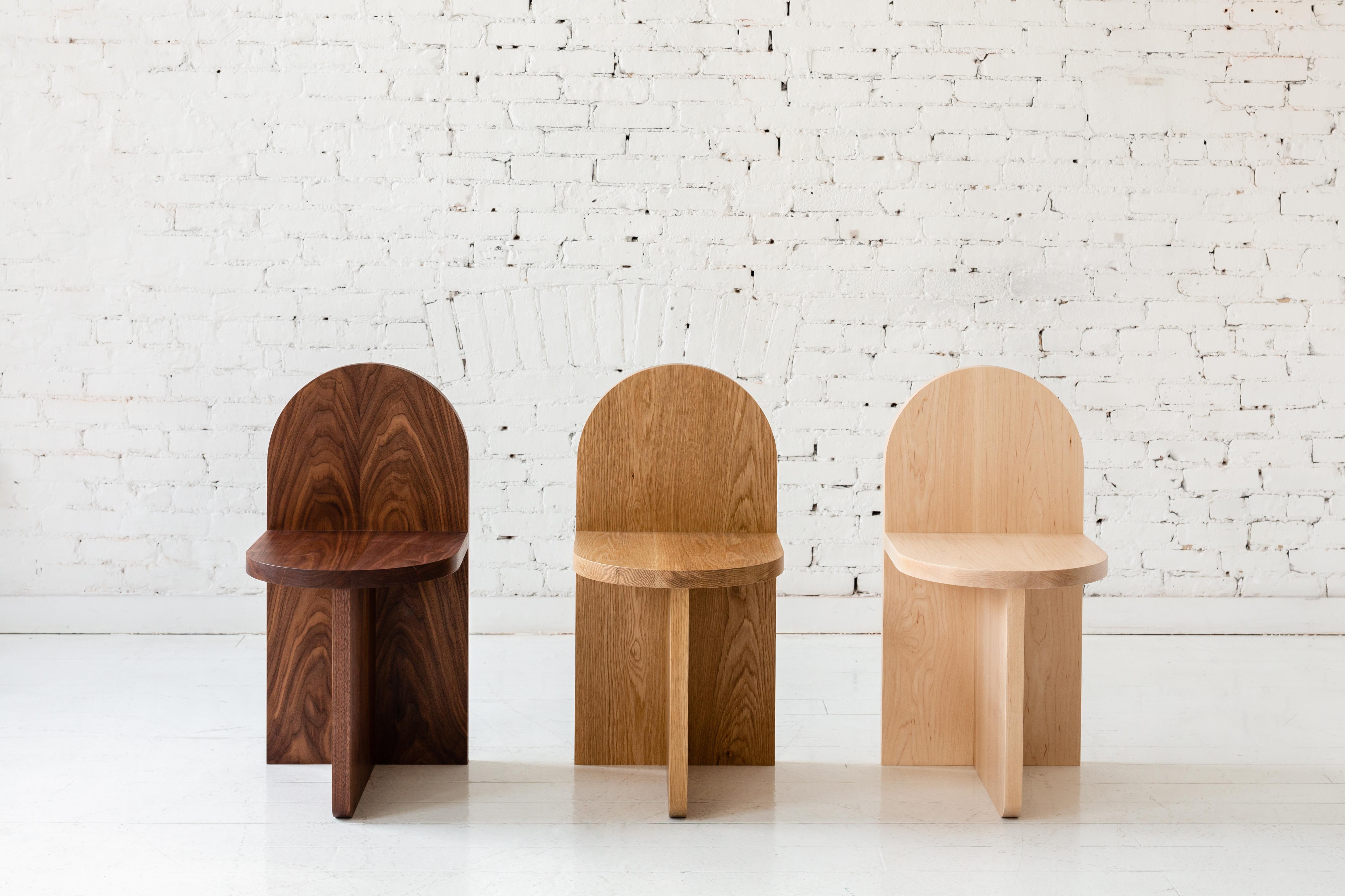 Cette chaise d'appoint minimale est composée de trois plans qui se croisent, le dossier ressemblant à une forme traditionnelle de pierre tombale. 

Disponible dans une variété de bois. Présenté en noyer, chêne blanc et frêne. Également disponible en