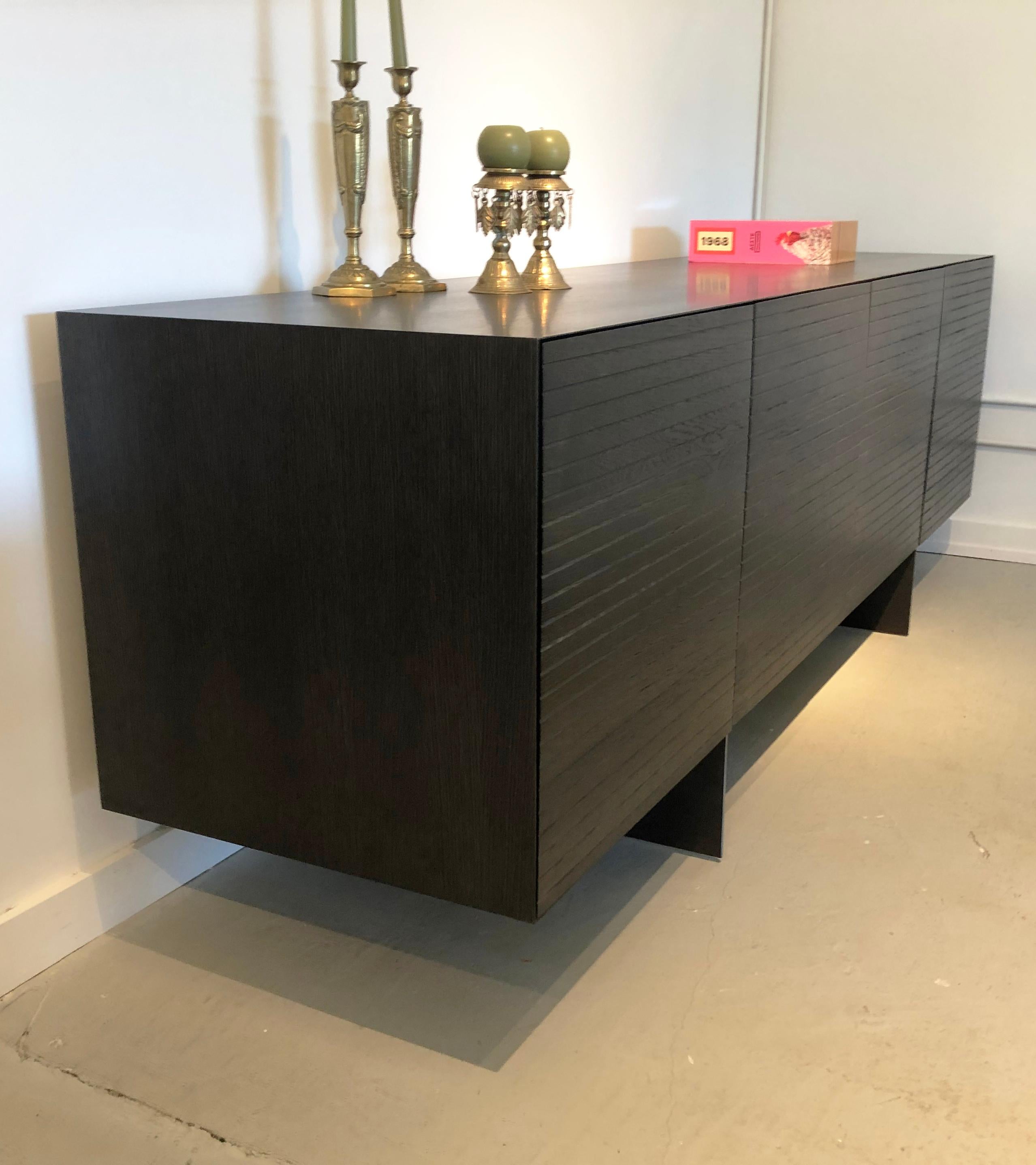 Custom made solid dark grey stained oak credenza with beveled edges, legs in solid raw steel. The doors have a pattern ridge repeating approximately every 1 inch. 4 solid doors with beveled edges, 120 degree hinges. One internal shelf in each