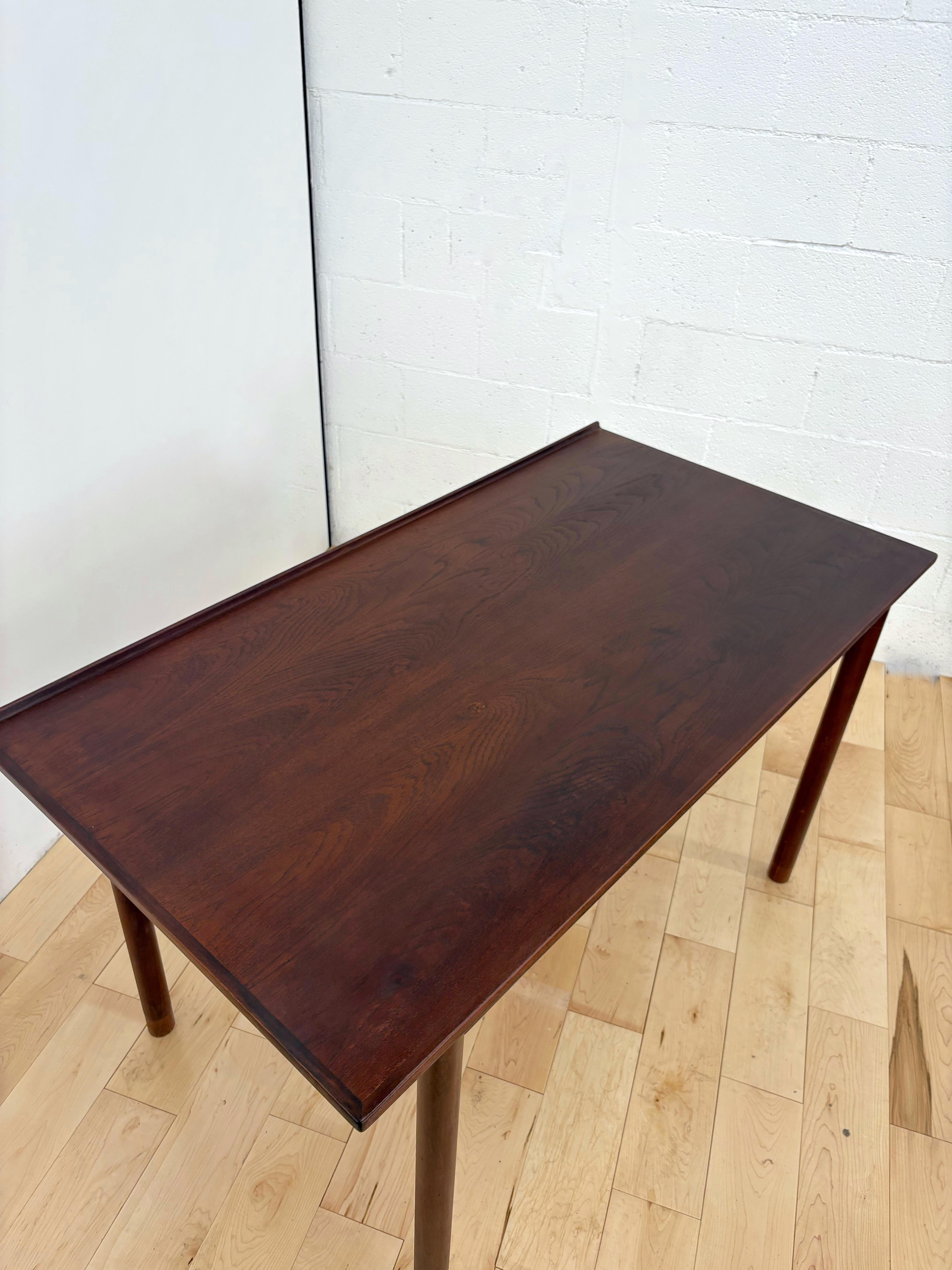 Raffinato esempio di design scandinavo del Mid-Century Modern, questo scrittoio di Hans Olsen incarna l'eleganza minimalista. Realizzata in noce scuro e teak, la scrivania presenta una superficie in teak incorniciata da un elegante bordo in noce,