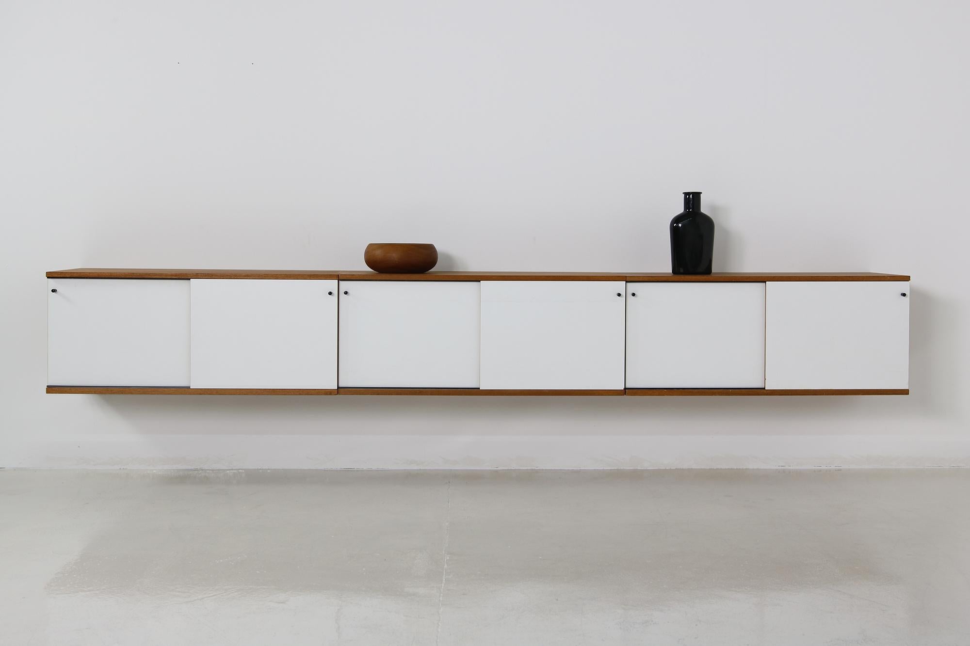 Rare 1960s teak sideboard system, wall-mounted, 3 parts, each one ca. 95 x 40 x 40 cm overall ca. 285 x 40 x 40 cm with white laminated sliding doors, black handles, two of them with a shelf inside, good vintage condition, beautiful Minimalist and