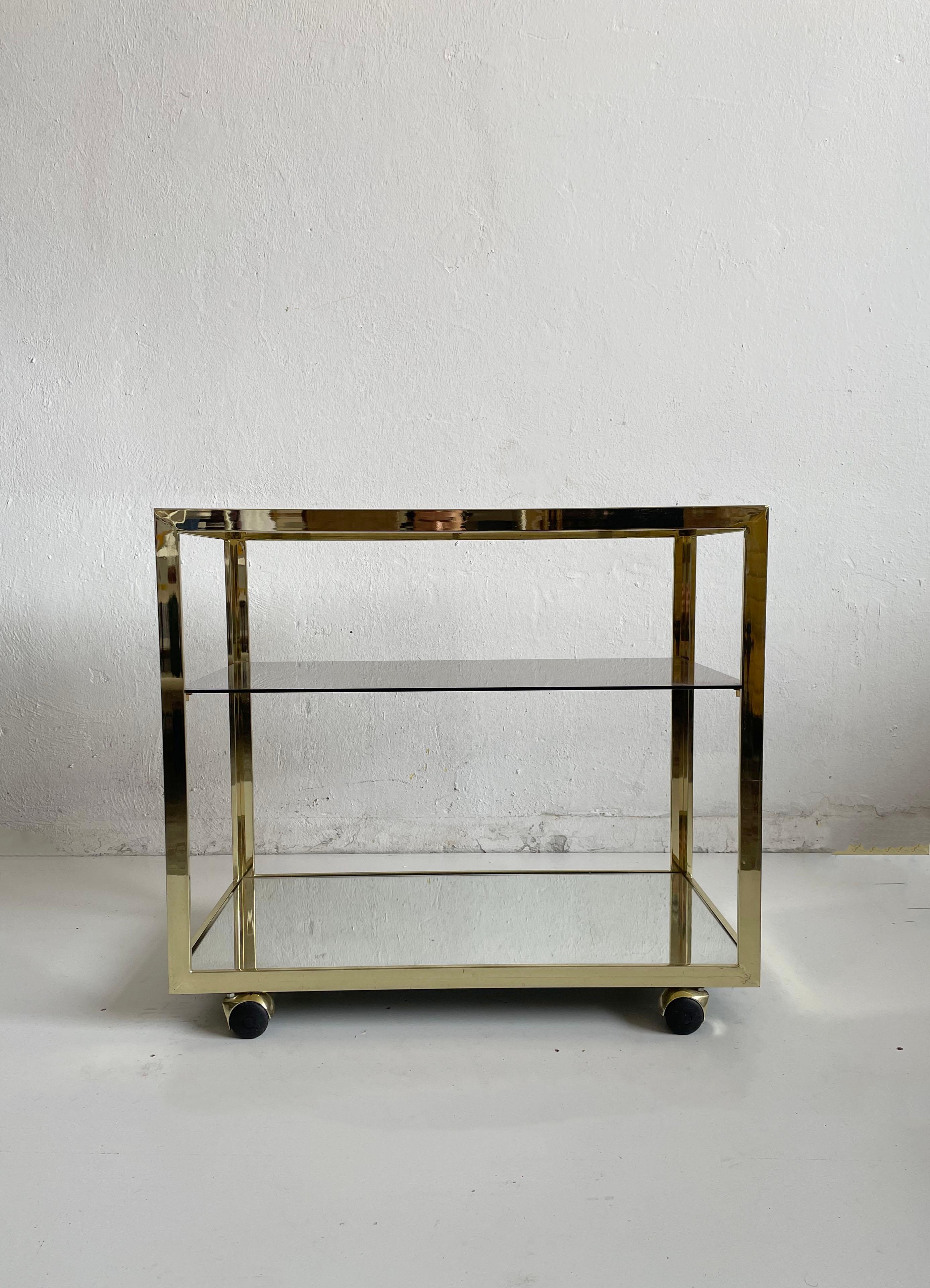 Chariot de bar minimaliste très élégant avec trois étagères en verre et cadre en métal plaqué laiton.
L'une des étagères en verre est en verre miroir, les deux autres sont en verre teinté.

La structure est très solide, le verre sans dommage,