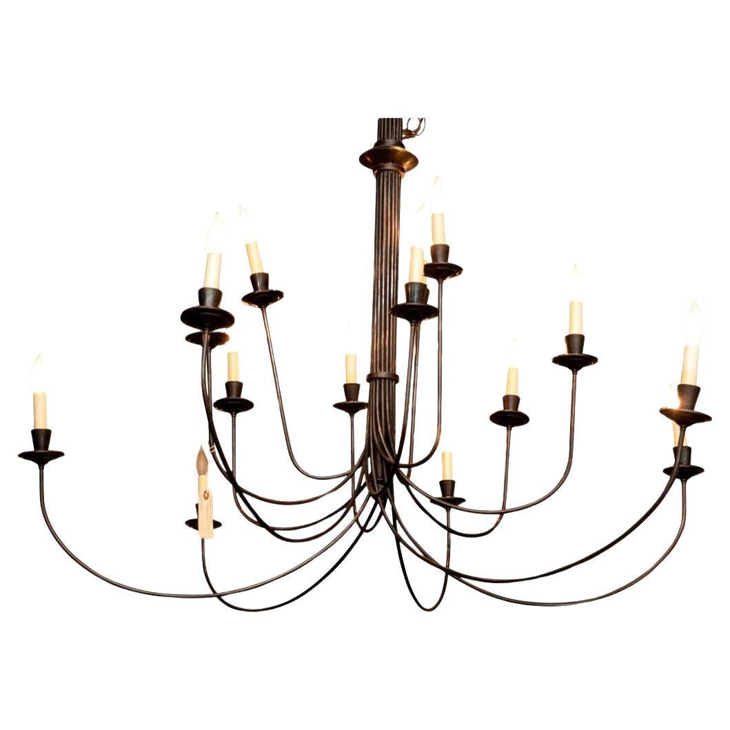 A Minimalist and sculptural Chandelier in bundled and sweeping Iron rods. Three tiers of thin arched black metal arms that are gathered together to form the tall ribbed standard. Tapered light sockets and saucer bobeches.  Lacking a ceiling canopy.