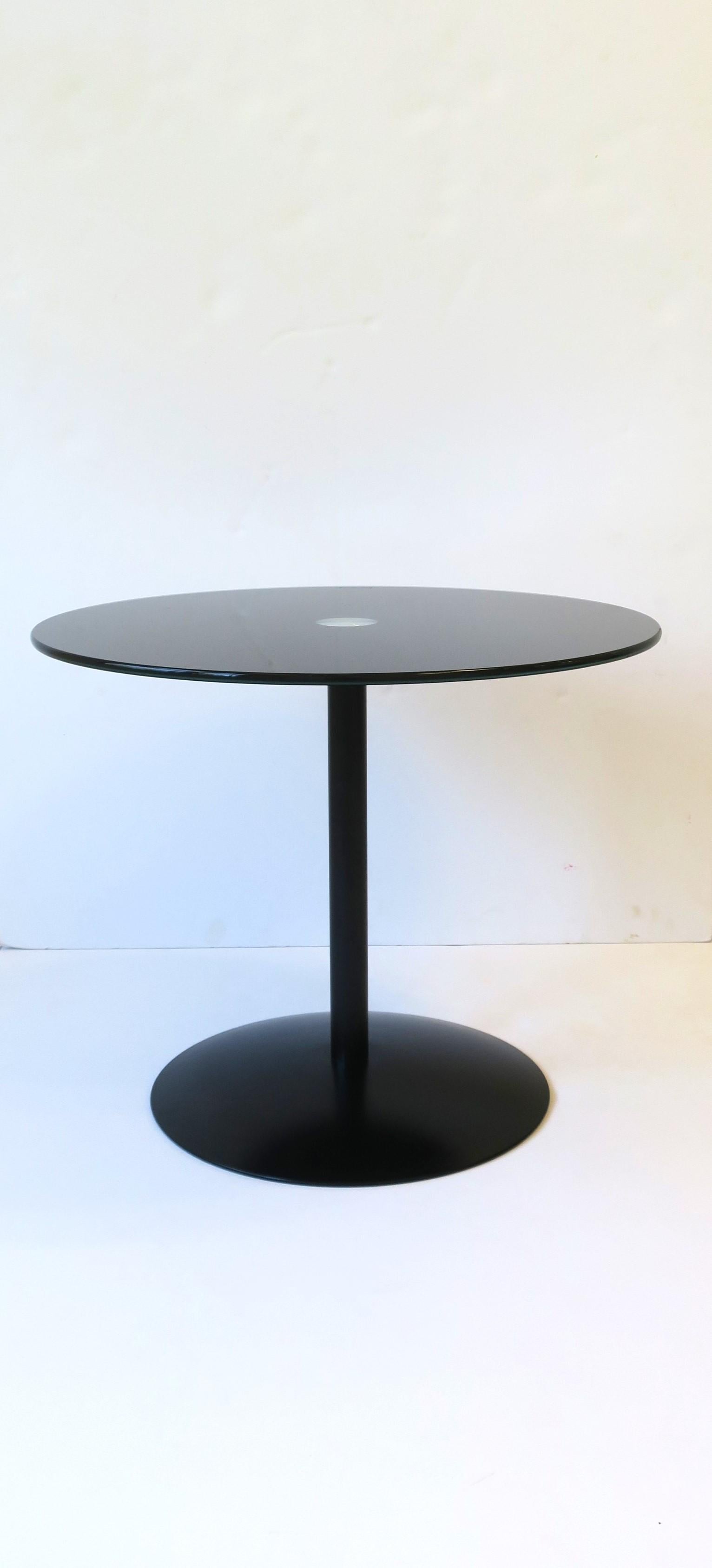 A beautiful and chic black glass and metal drinks side table in the Minimalist modern style, circa early 21st century. Table has a black glass top and metal base. Table's top resembles an LP record album with its jet-black color, circular shape, and