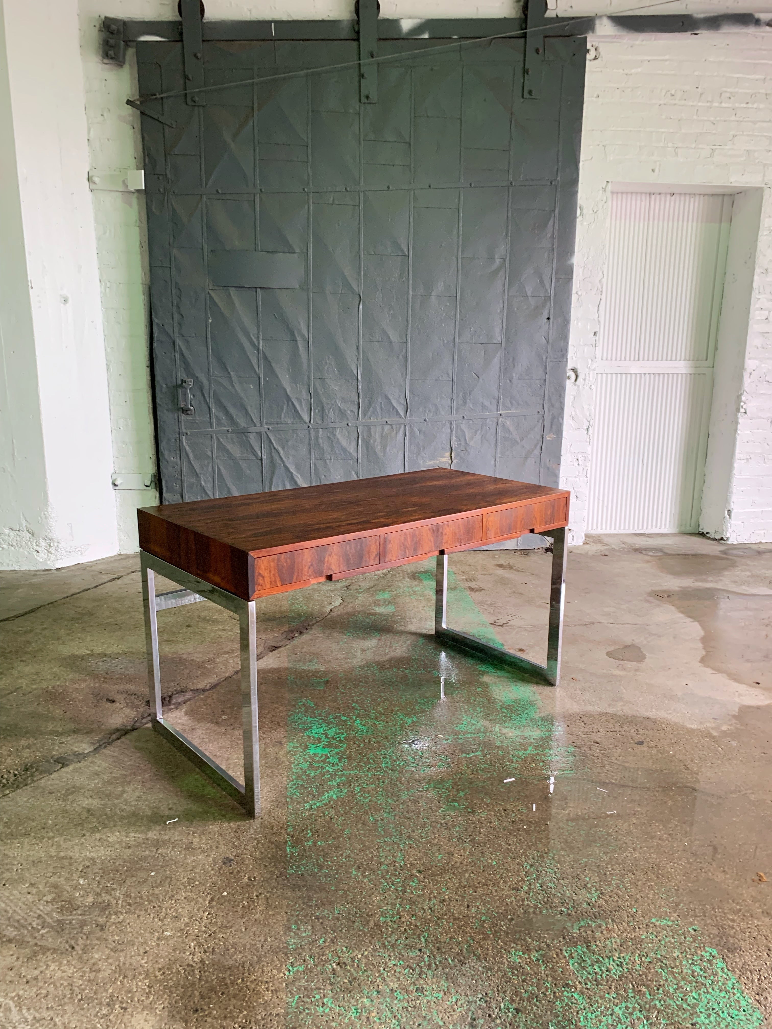 Incredibly stunning Danish minimalist desk, with a style calling to mid-century modern icon Milo Baughman, c.1970s.

Rich Brazilian rosewood grain, supported by a sturdy chrome base. The desk features three drawers for storage, with a cut detail