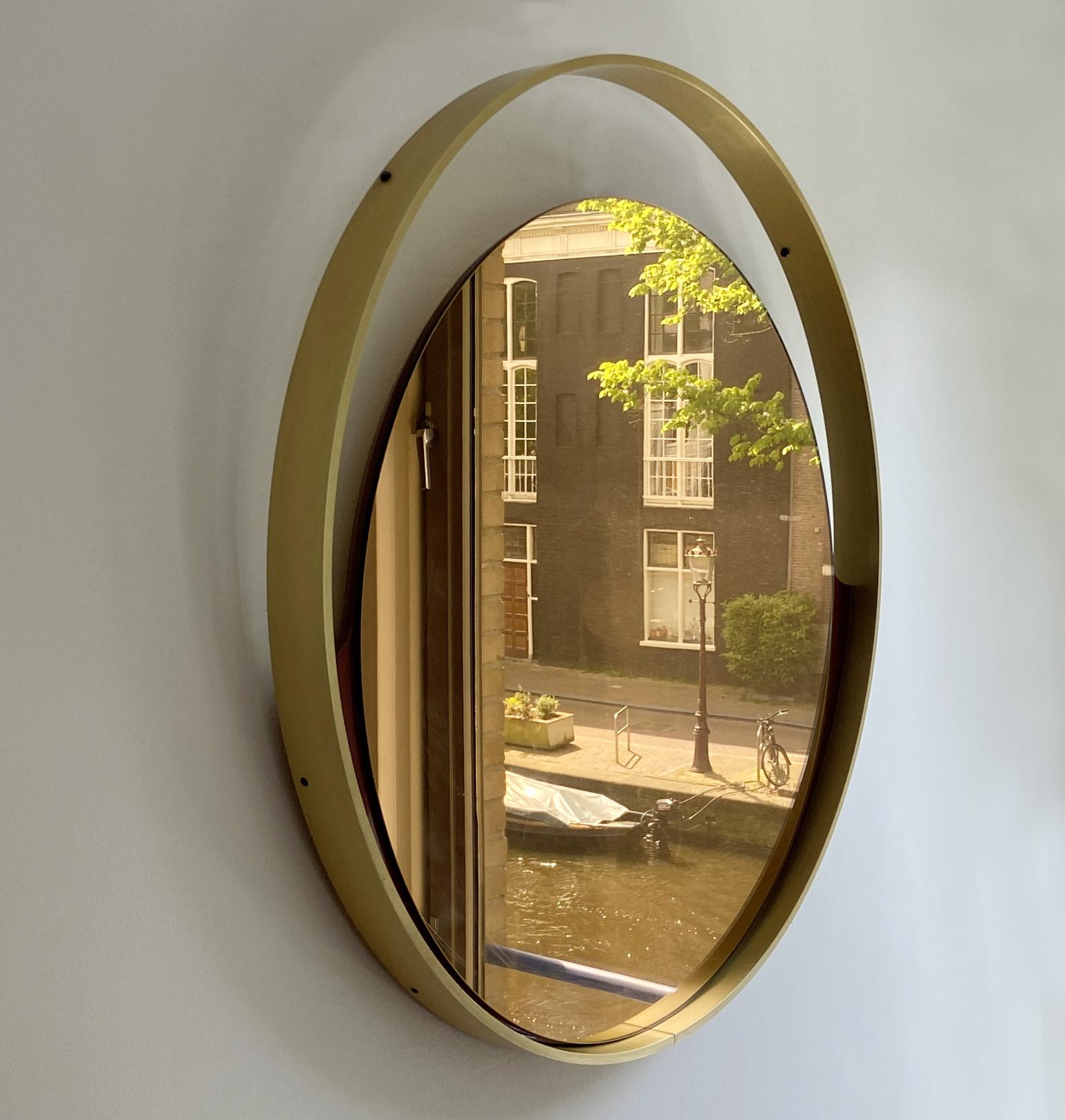 Miroir rond minimaliste en bronze légèrement teinté de la société italienne Rimadesio. La bordure en aluminium est anodisée en or et contient un miroir en bronze qui descend comme un coucher de soleil. Il est relié au cadre par deux ailes émaillées