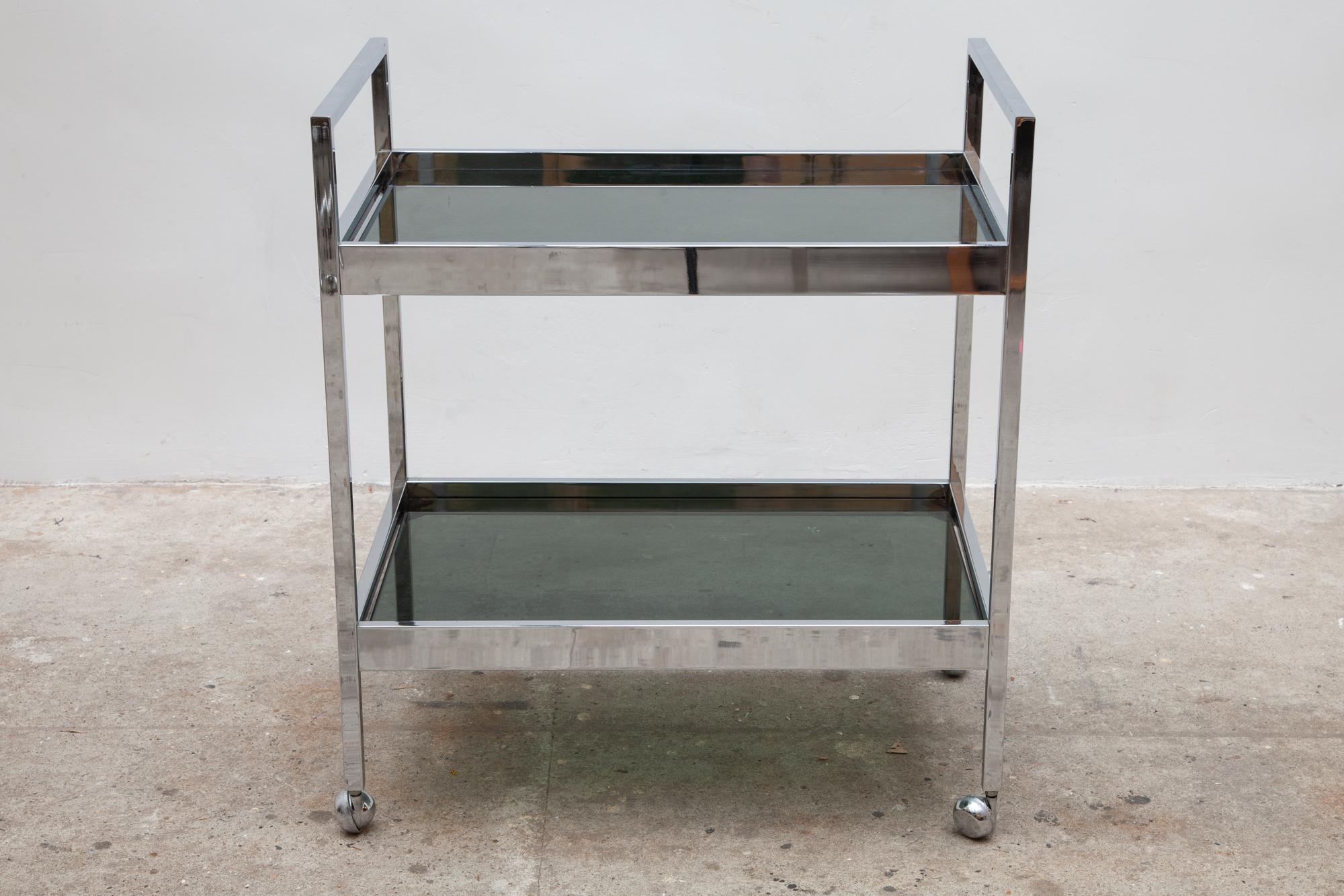 Minimalist bar cart with two smoked glass shelves and chrome metal frame. The structure is very sturdy, glass without damage. This trolley is in fully working order as intended and in very good original condition.