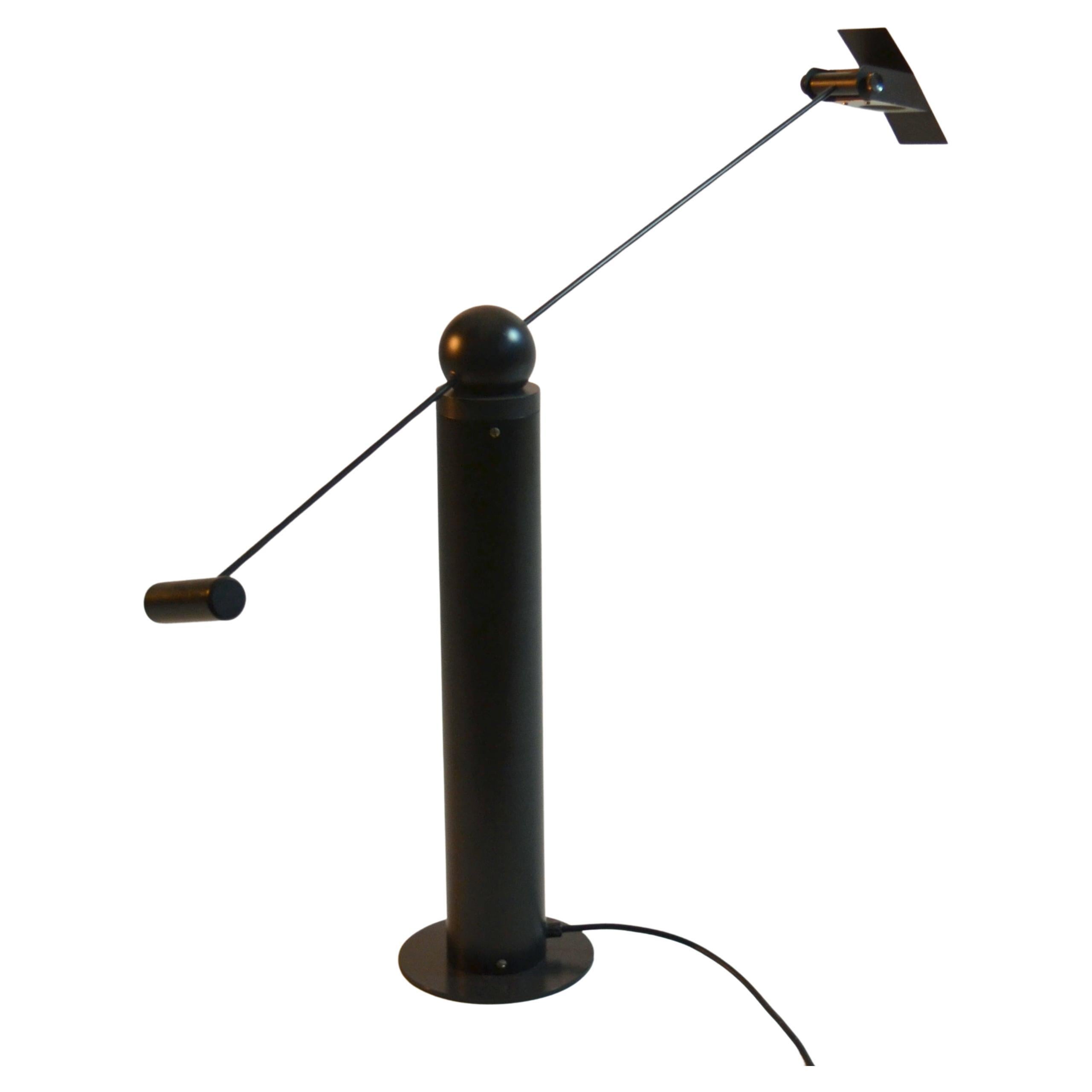 Minimal black metal table lamp with adjustable arm counterbalancing on cylinder base and halogen light source attributed to Rico & Rosemarie Baltensweiler, Switzerland 1970's. The lamp balances on a ball weight resting on a pillar base that allows