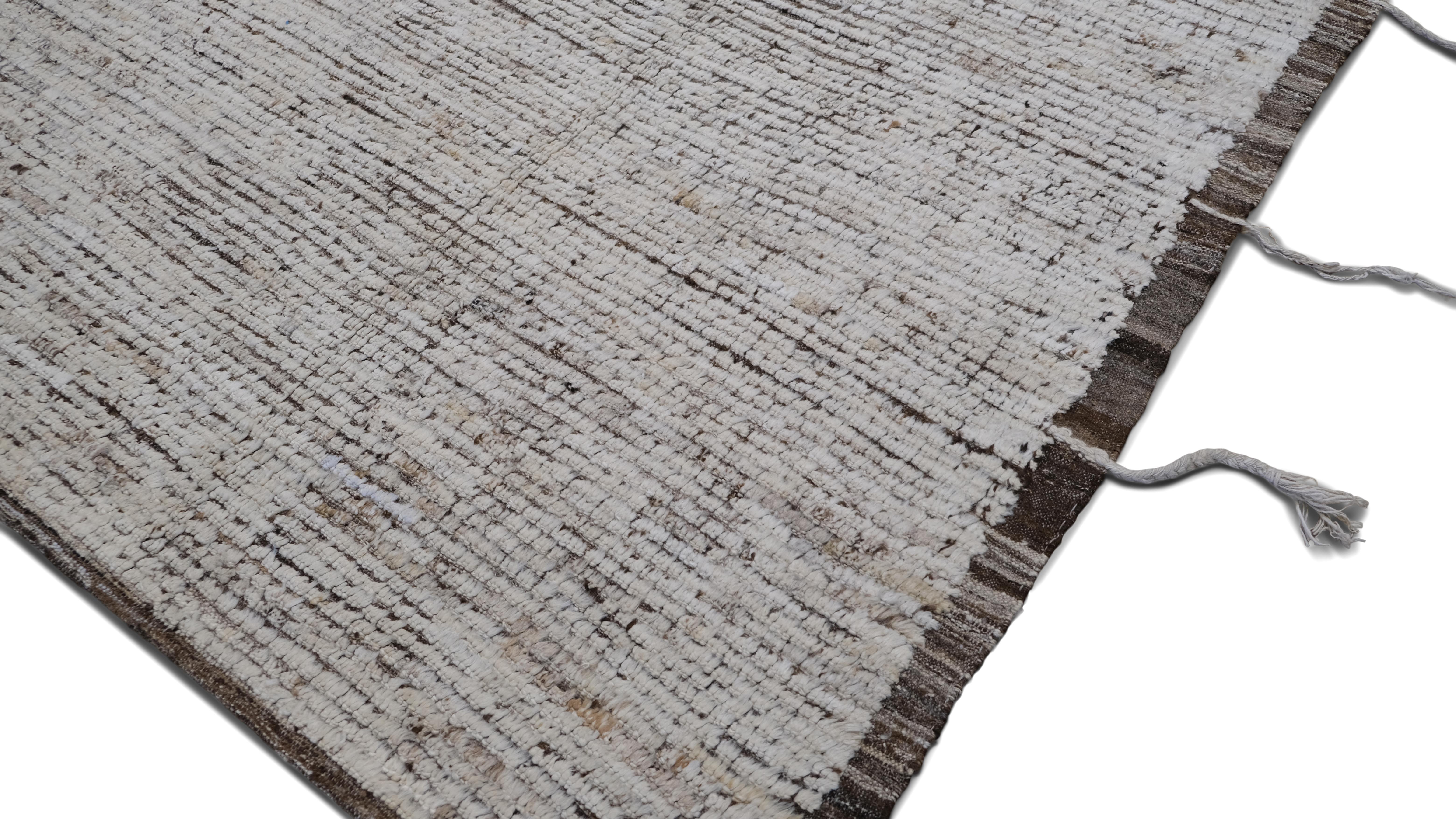 Questo tappeto in lana annodato a mano presenta un'estetica organica e testuale ispirata ai tradizionali intrecci tribali. Caratterizzato da una palette di colori neutri con sottili variazioni di tono, questo pezzo incarna una sobria eleganza e una