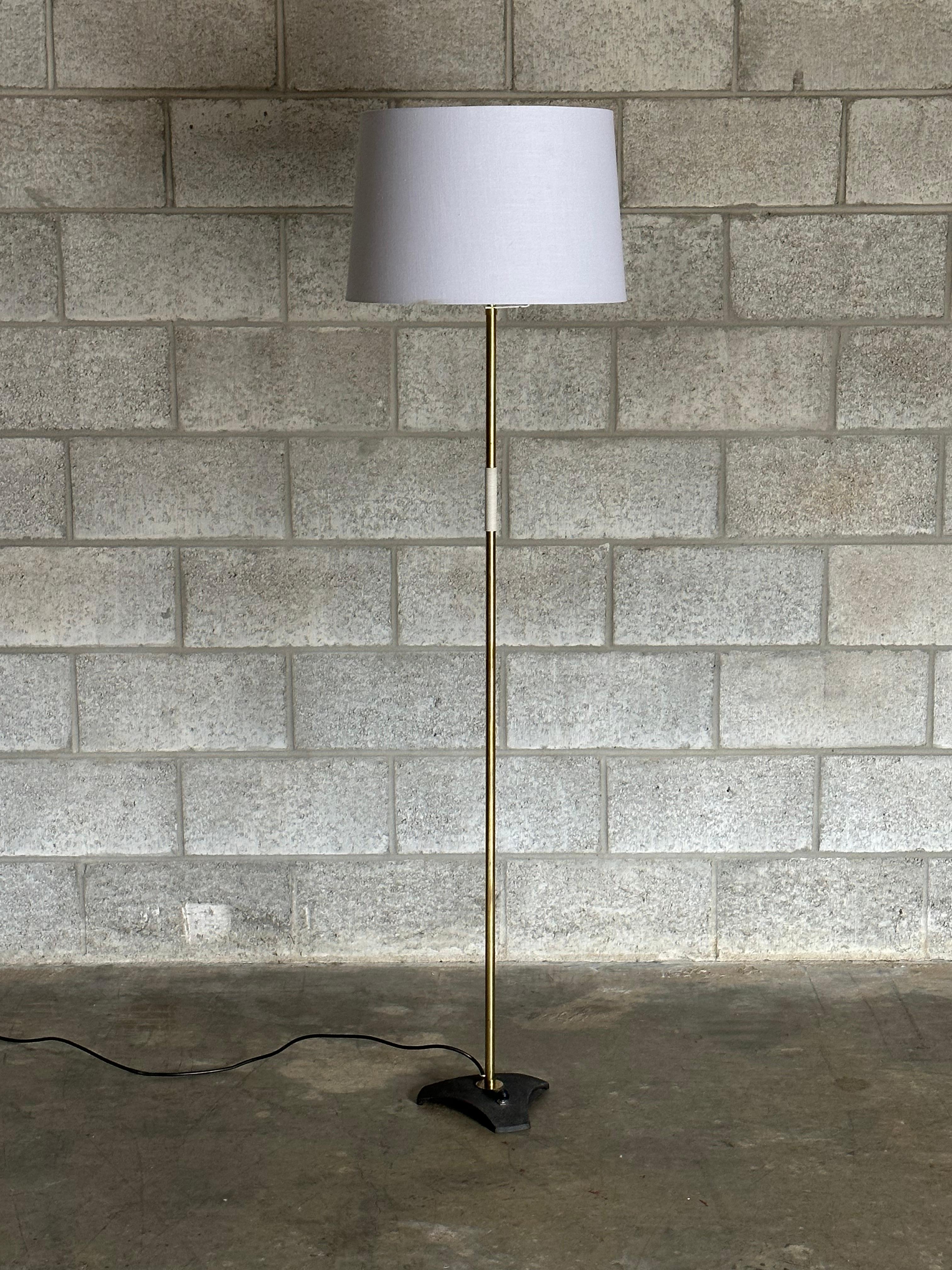 A wonderful minimalist floor lamp by Rupert Nikoll. Features a cast iron base with thin brass plated tubing, a section wrapped in, what appears to be, nylon, and finally a classic shade. Great minimalist form, with a push through socket and a foot