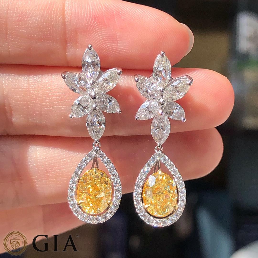 We invite you to discover this unique pair of minimalist earrings set with GIA certified oval cut Fancy Yellow diamonds of 2.84 carats enhanced with a halo of colorless diamonds as well as approximately 2ct marquise cut diamonds. These beauties
