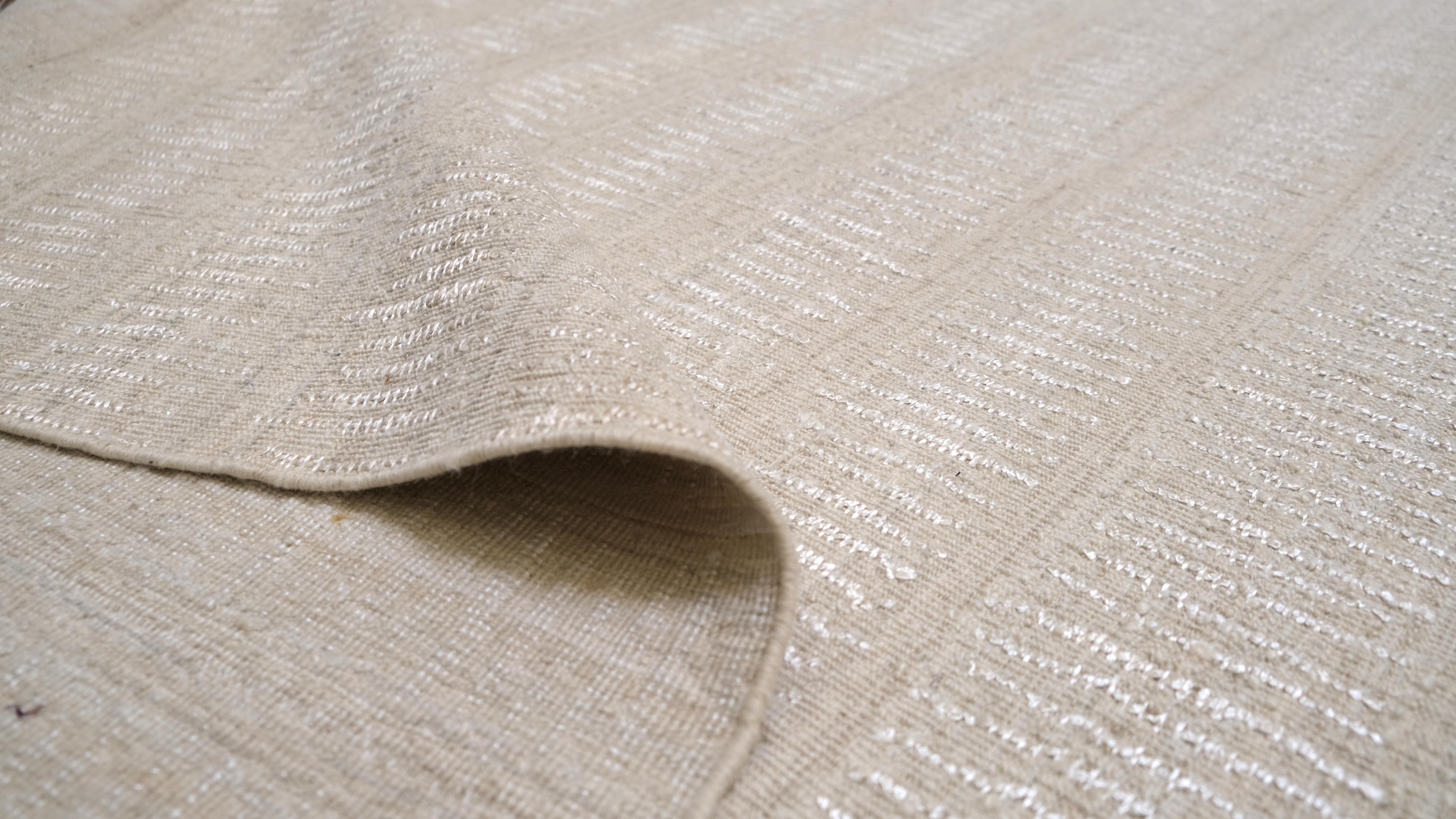 Dieser handgeknüpfte Wollteppich ist ein Beispiel für die Schönheit des modernen Minimalismus mit seinem eleganten und zurückhaltenden Design. Mit seiner subtilen, horizontal gestreiften Textur fängt die Oberfläche des Teppichs sanft das Licht ein
