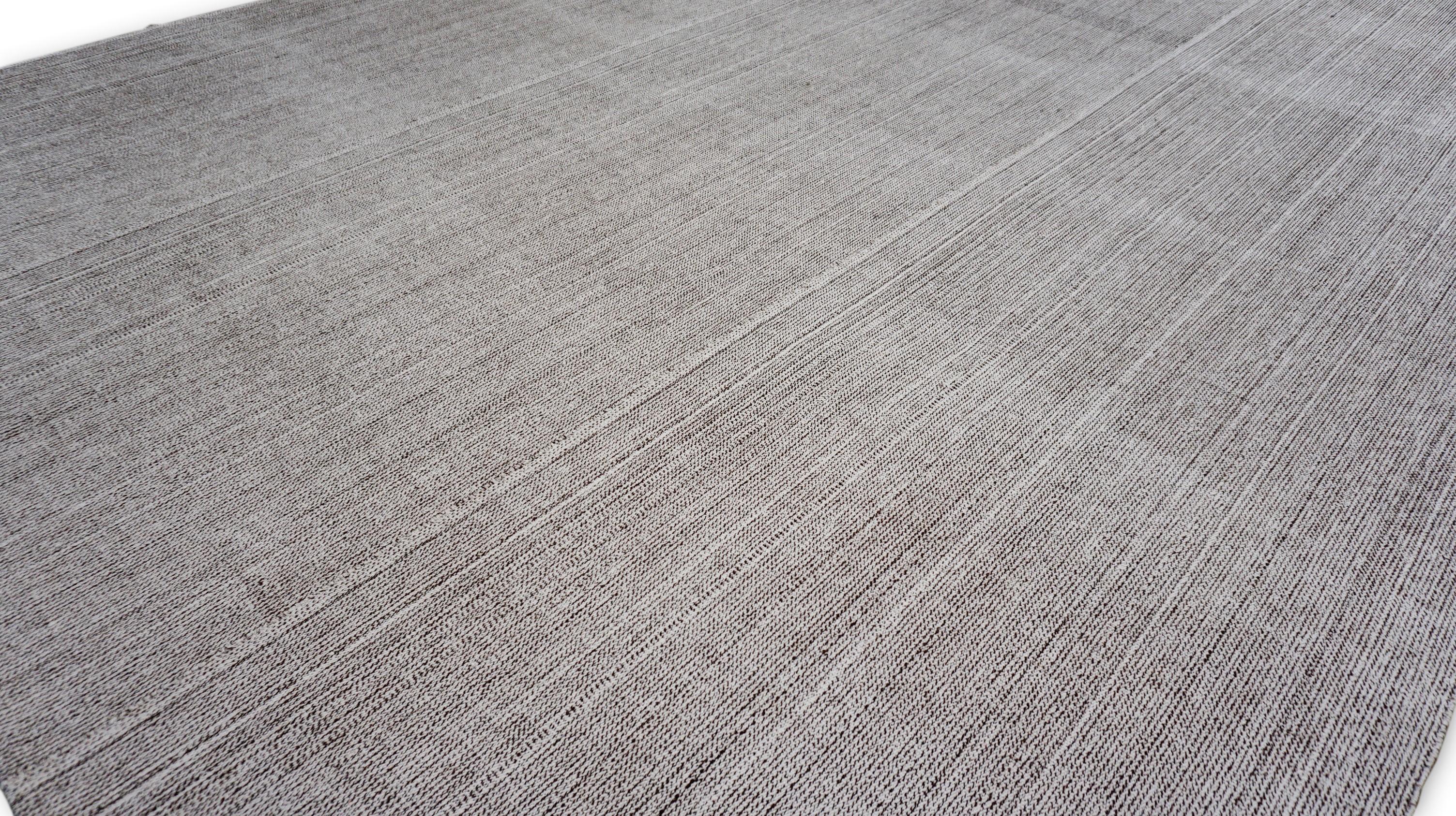 This hand-woven wool rug features a refined linear stripe pattern, delicately woven in a soft gray palette with ivory and tan tonal variations. The understated design creates a calming and sophisticated aesthetic, making it an ideal choice for