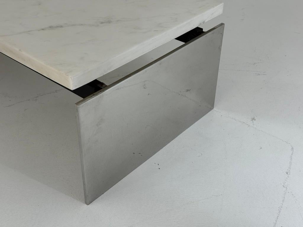 Questo straordinario tavolo da cocktail offre una masterclass di raffinato minimalismo, abbinando la fresca eleganza del marmo bianco alla raffinatezza industriale dell'acciaio lucido. Il piano rettangolare in marmo, sottilmente levigato per