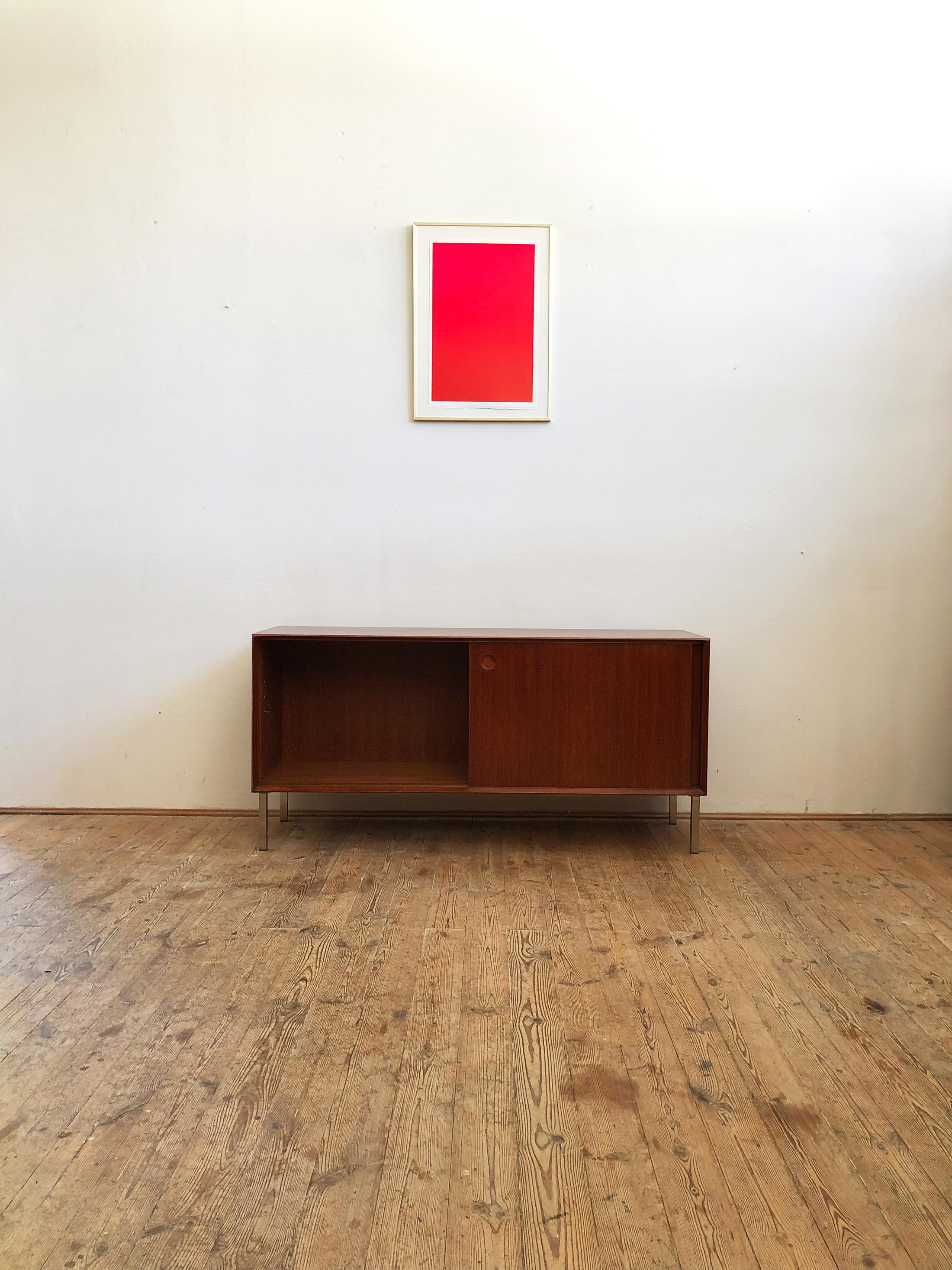 This Minimalist midcentury teak sideboard was designed by Walter Wirz and manufactured in Germany.

The sideboard is made of Mahagoni-colored teak veneer on chrome feet which were added later on and shows beautiful details, especially the handles