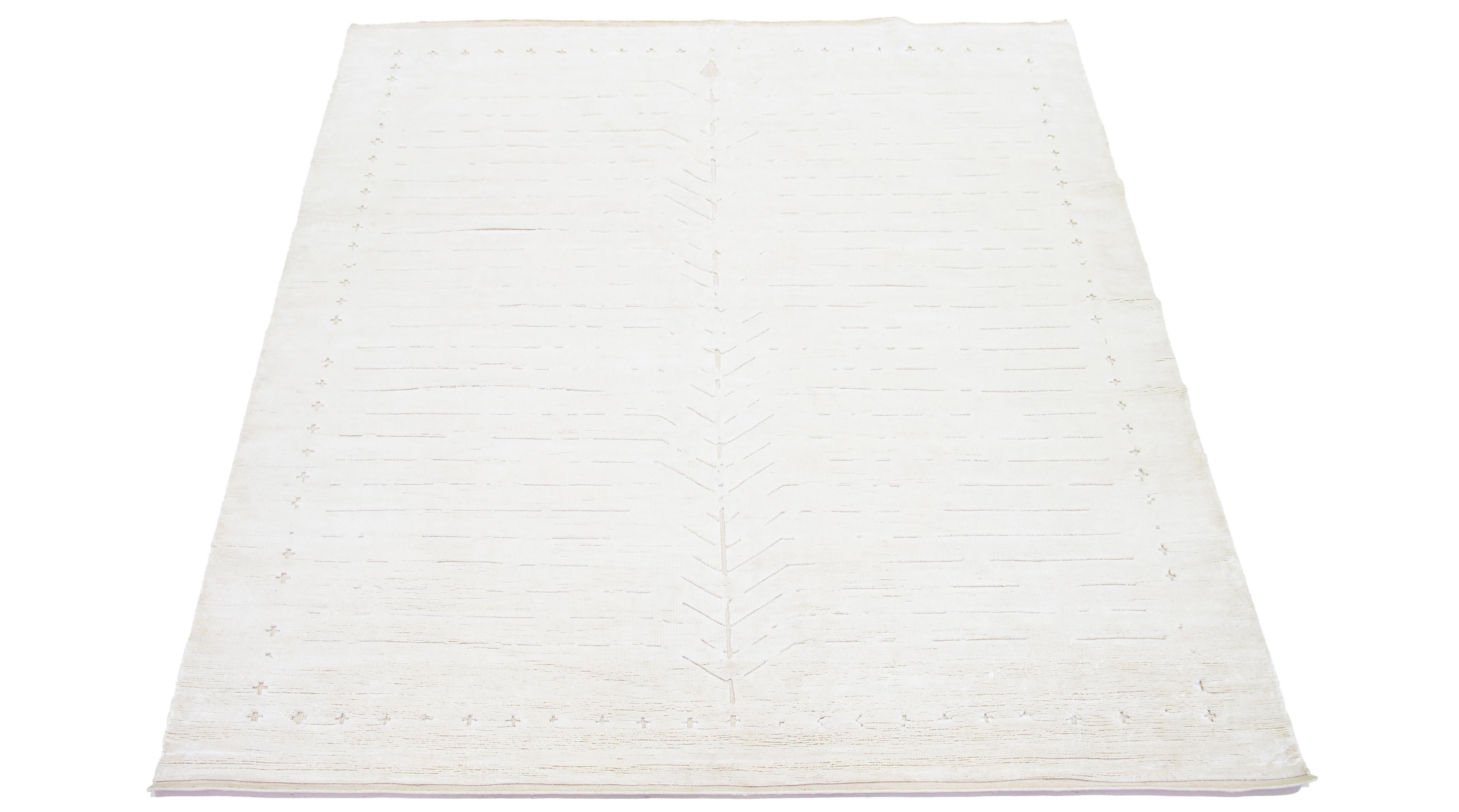 Questo tappeto in lana, sapientemente annodato a mano, presenta un design marocchino contemporaneo in toni beige tenui in contrasto con uno sfondo avorio di grande effetto, per una presentazione minimalista.

Questo tappeto misura 8'1
