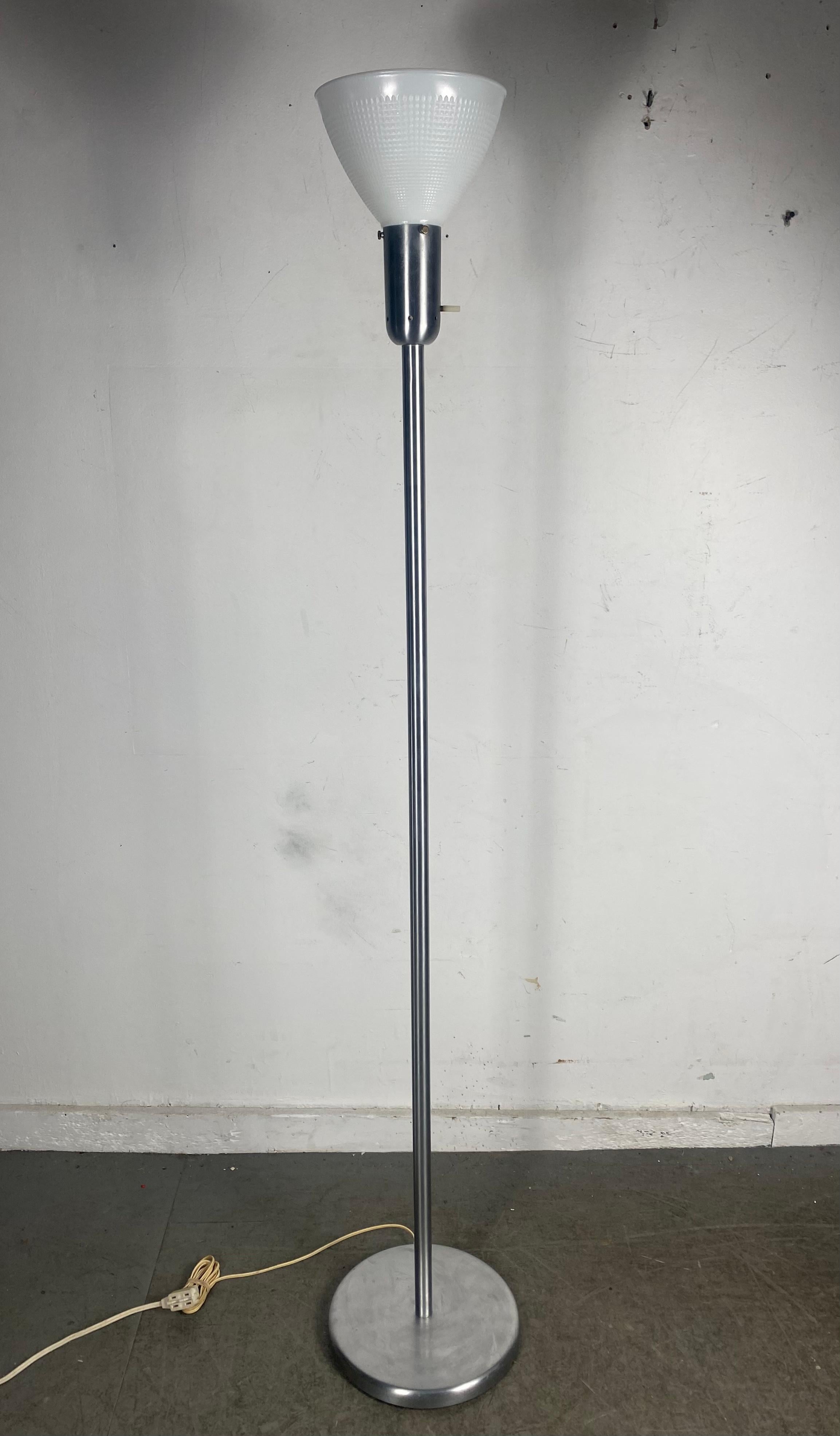 Classic Modernist floor lamp. Simple elegant design from Nessen Studios.Ny. Lamp has a brushed nickel finish. Round base. Standard stem// Retains its original ribbed plastic (bakelite) stem. On/off switch. Elegant, modern simplicity that works in