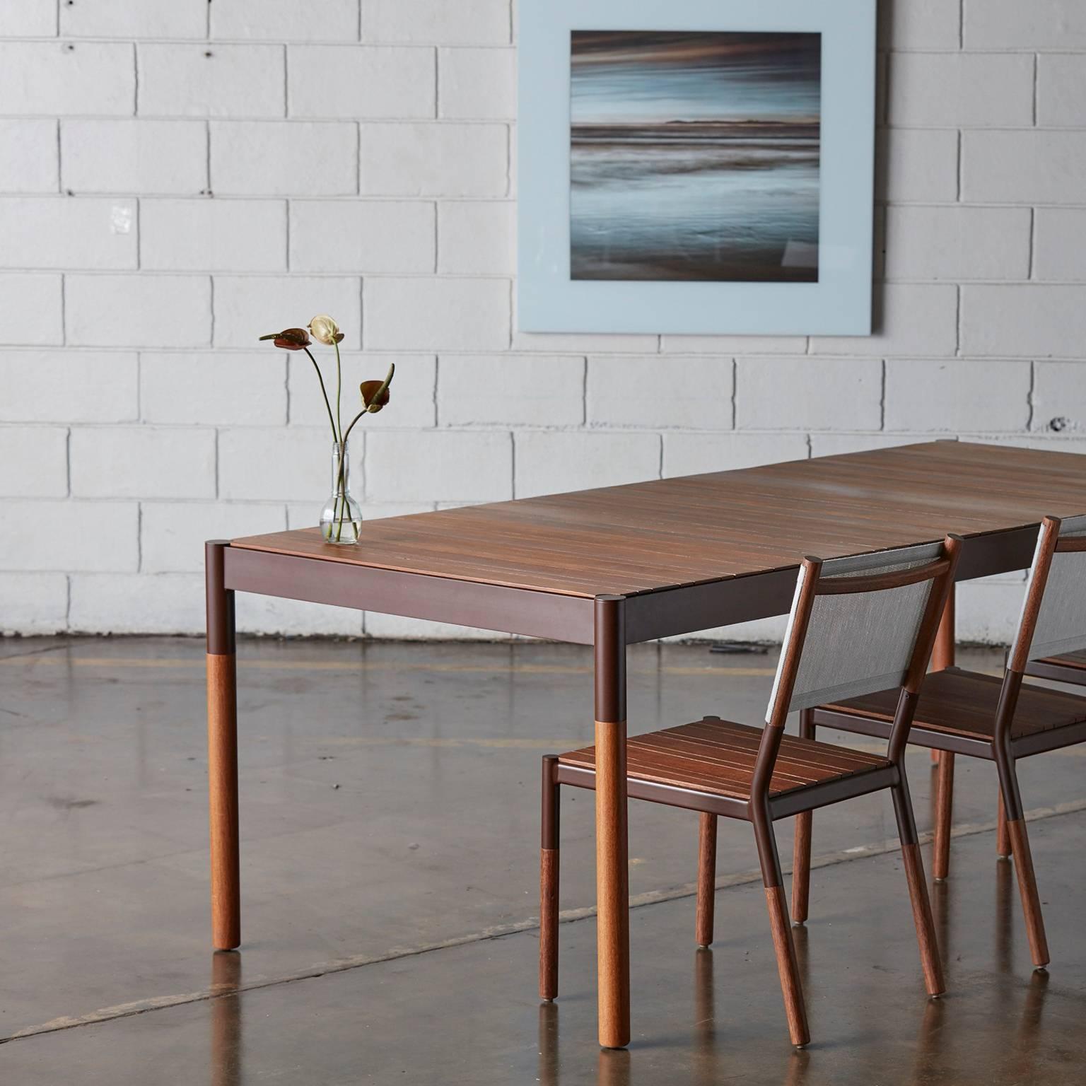 Dieser Esstisch für den Außenbereich ist aus Hartholz und Metall in einem minimalistischen Design gefertigt. Es ist ein Tisch, der eine dünne Massivholzplatte mit einem robusten Korpus kombiniert, der das sanfte und weiche Aussehen der Platte mit