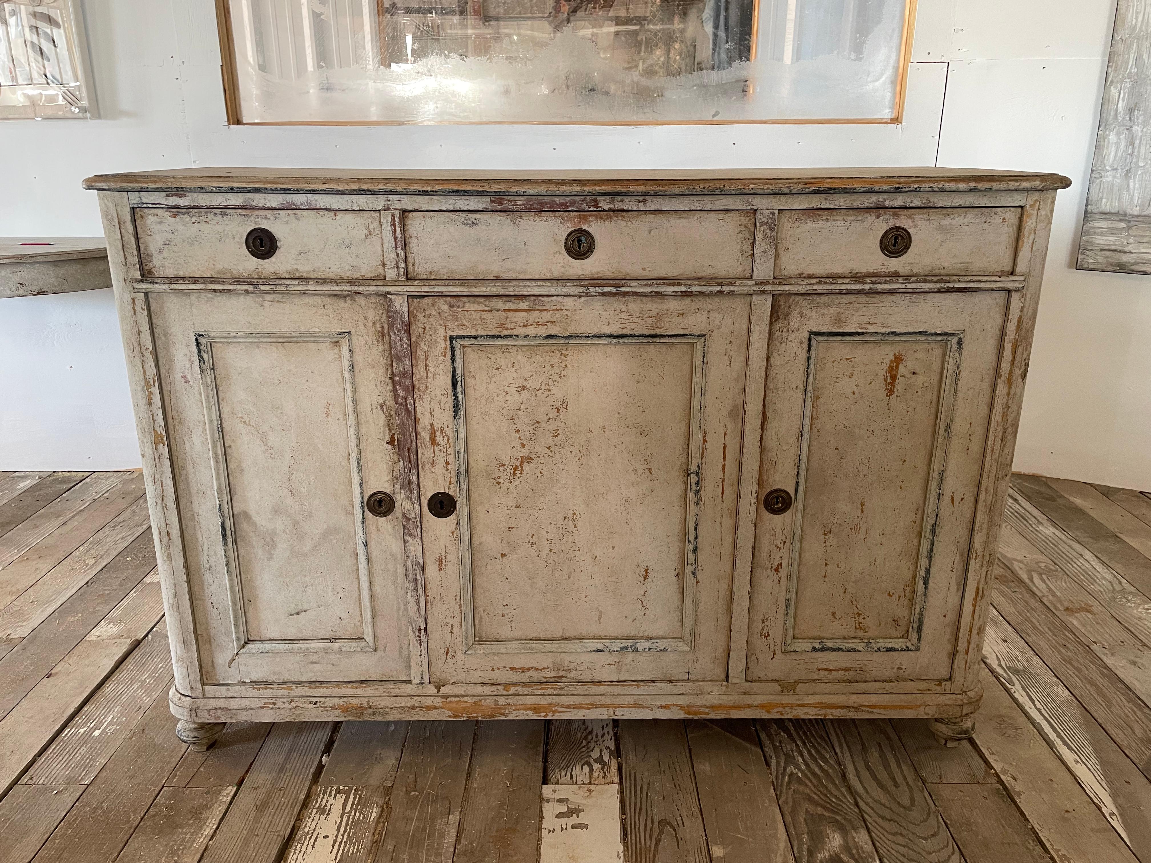 Here is a beautiful imported Swedish 3 door, 3 drawer sideboard that is dry scraped and painted to a beautiful neutral tone with whites/creams. This is a fantastic minimalist piece that can go in many different design spaces. It is truly one of a