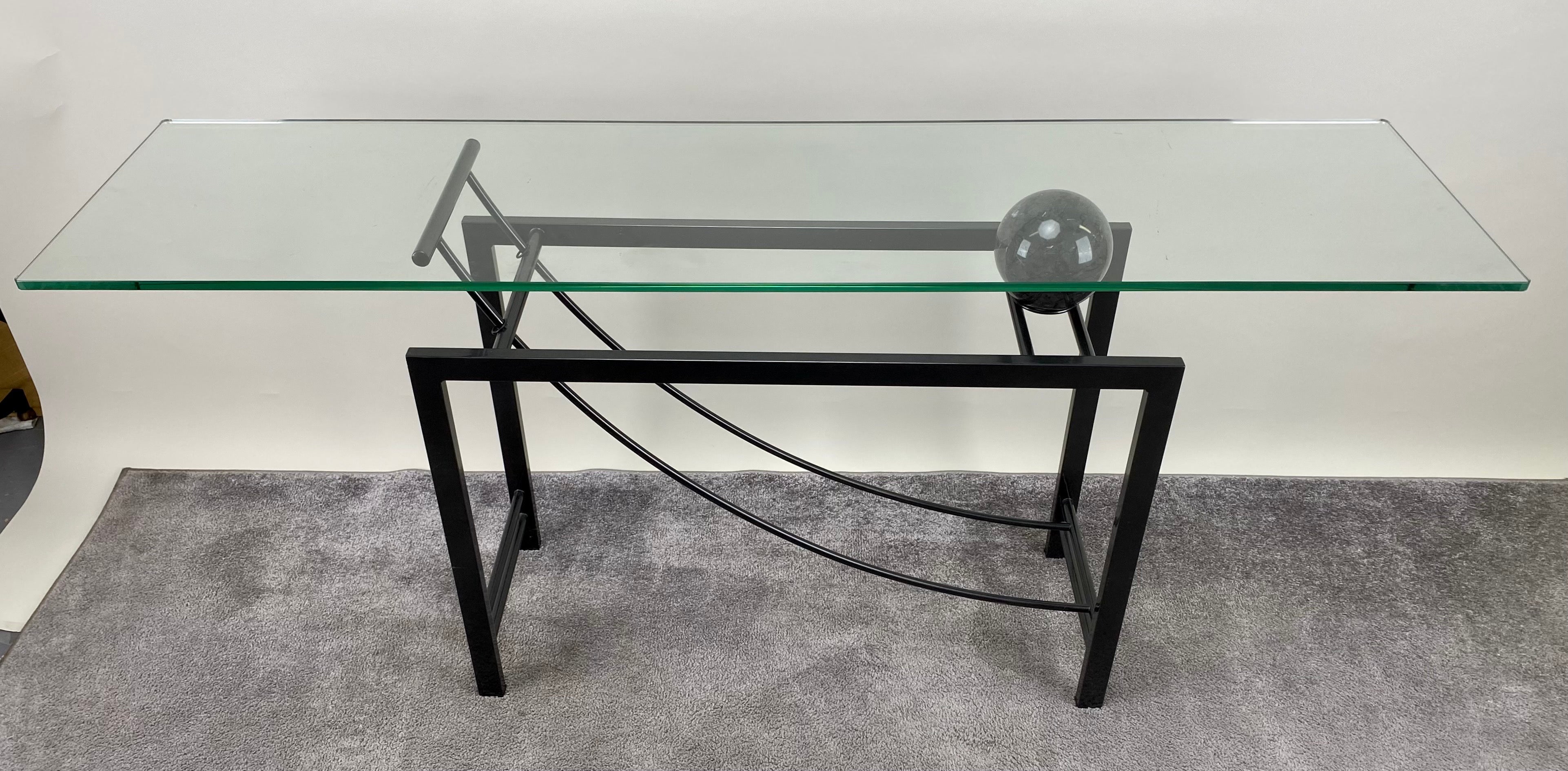
Introducing an exquisite minimalist console, a fusion of geometric elegance and sleek sophistication. Crafted from black metal, its clean lines form a striking structure crowned with a rectangular glass top. A defining feature of this console is a