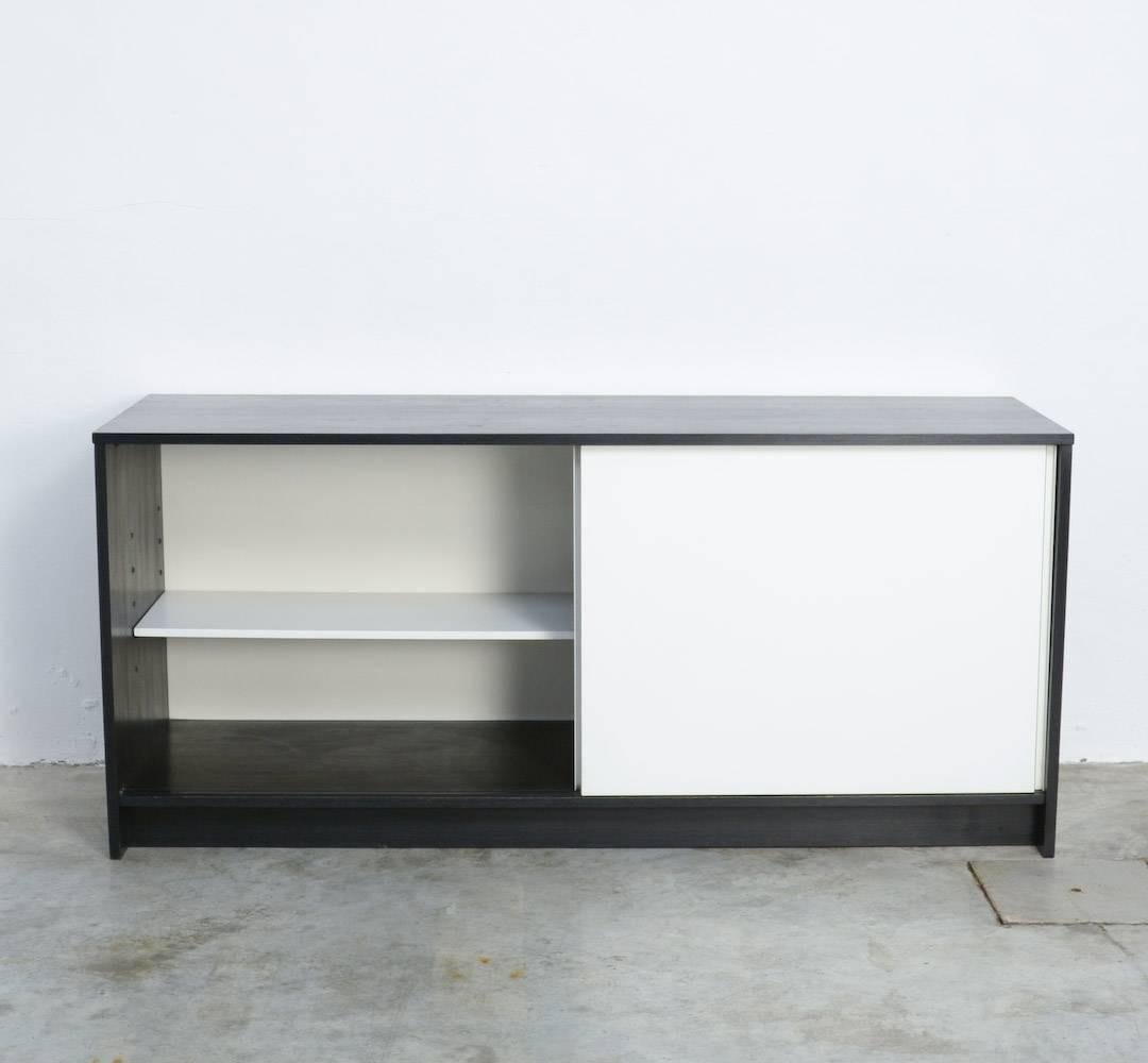 This Minimalist sideboard, model KW90, was designed by Martin Visser for ’t Spectrum, in 1965.
The black ebonized wood contrasts nicely with the white laminated sliding doors.
Inside there are two white shelves and a drawer.
This Minimalist