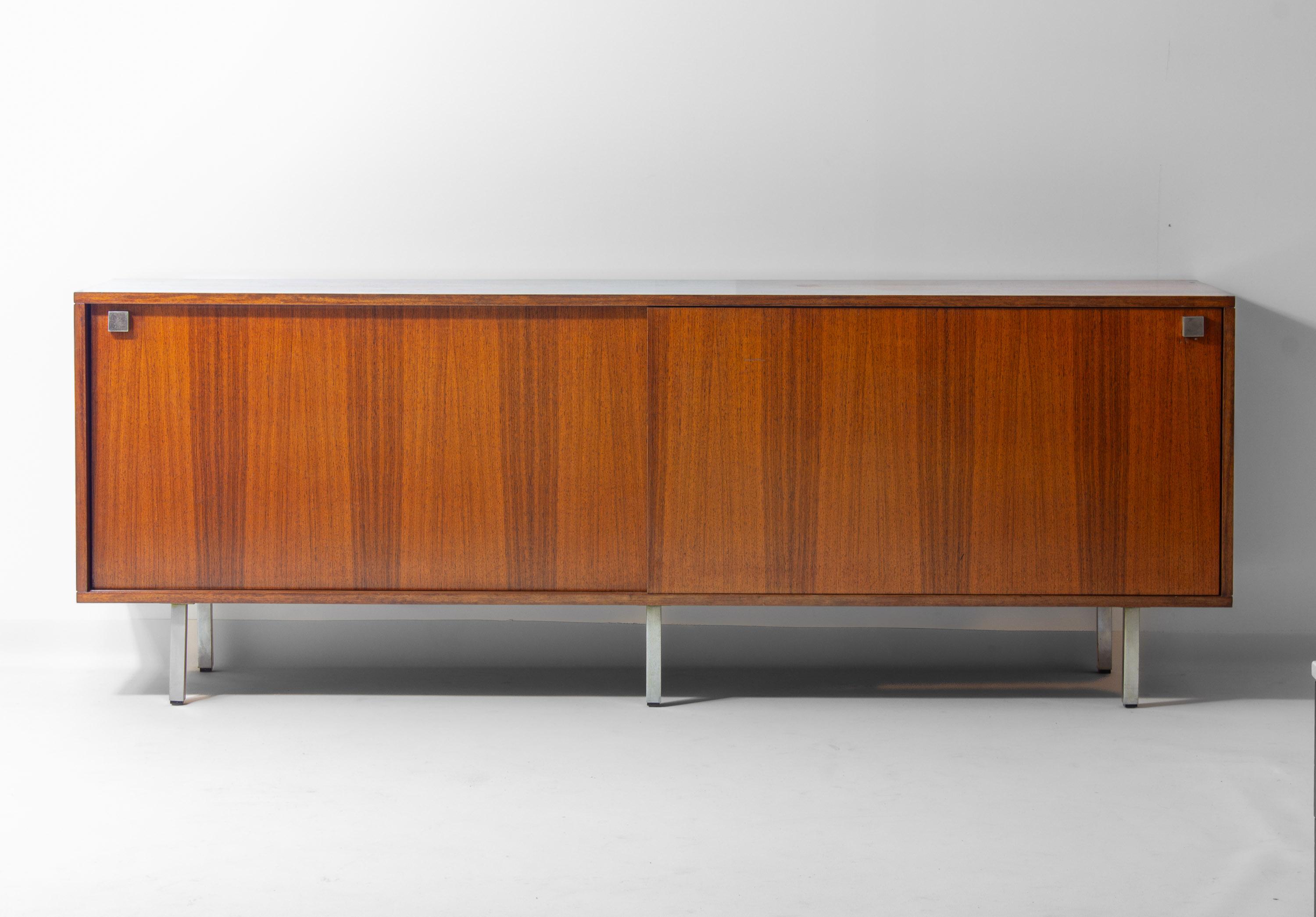 Minimalist sideboard designed by Alfred Hendrickx for Belform in the 1960s. It features two large sliding doors with square metal handles, opening to shelves and a drawer for practical storage. The sideboard stands on slim metal legs.