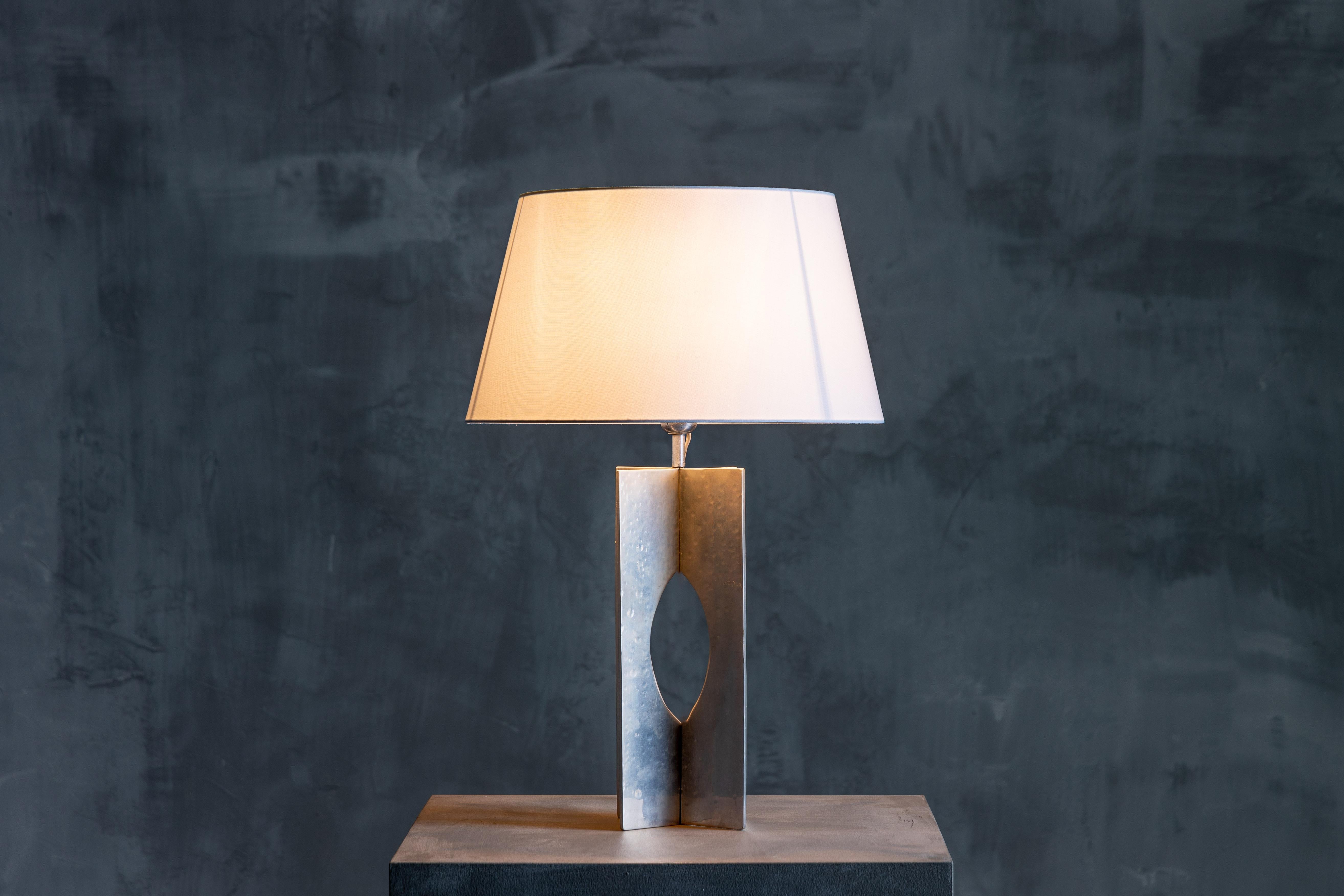 Minimalist table lamp in the style of George Kovacs. Crafted with a sleek chromed steel base, its understated design seamlessly blends into any interior aesthetic. Perfect for adorning console tables, this lamp embraces the beauty of imperfection