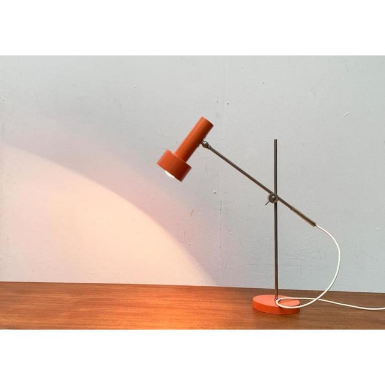 Minimalist Mid Century table lamp from Beisl in a special color.

The minimalist radiator shape of the light head is striking. Two simple cylinders of different sizes. The orange of the head is repeated in the heavy plate of the lamp. The spotlight
