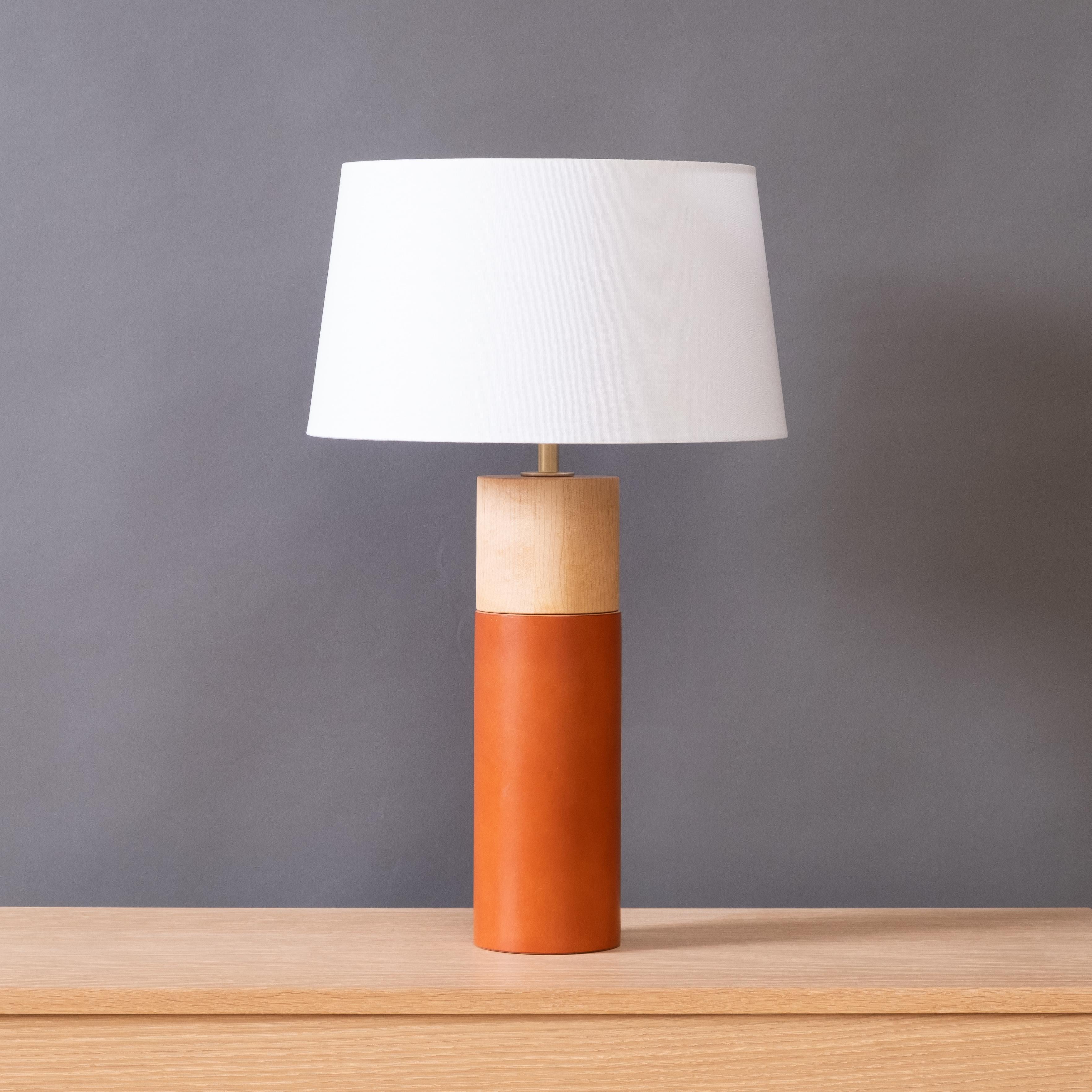 La lampe de table Capsule associe des formes minimalistes à des matériaux naturels richement texturés. Un cuir anglais épais enveloppe la partie inférieure du corps en bois tourné, contrastant avec le bois huilé exposé dans la partie supérieure. La