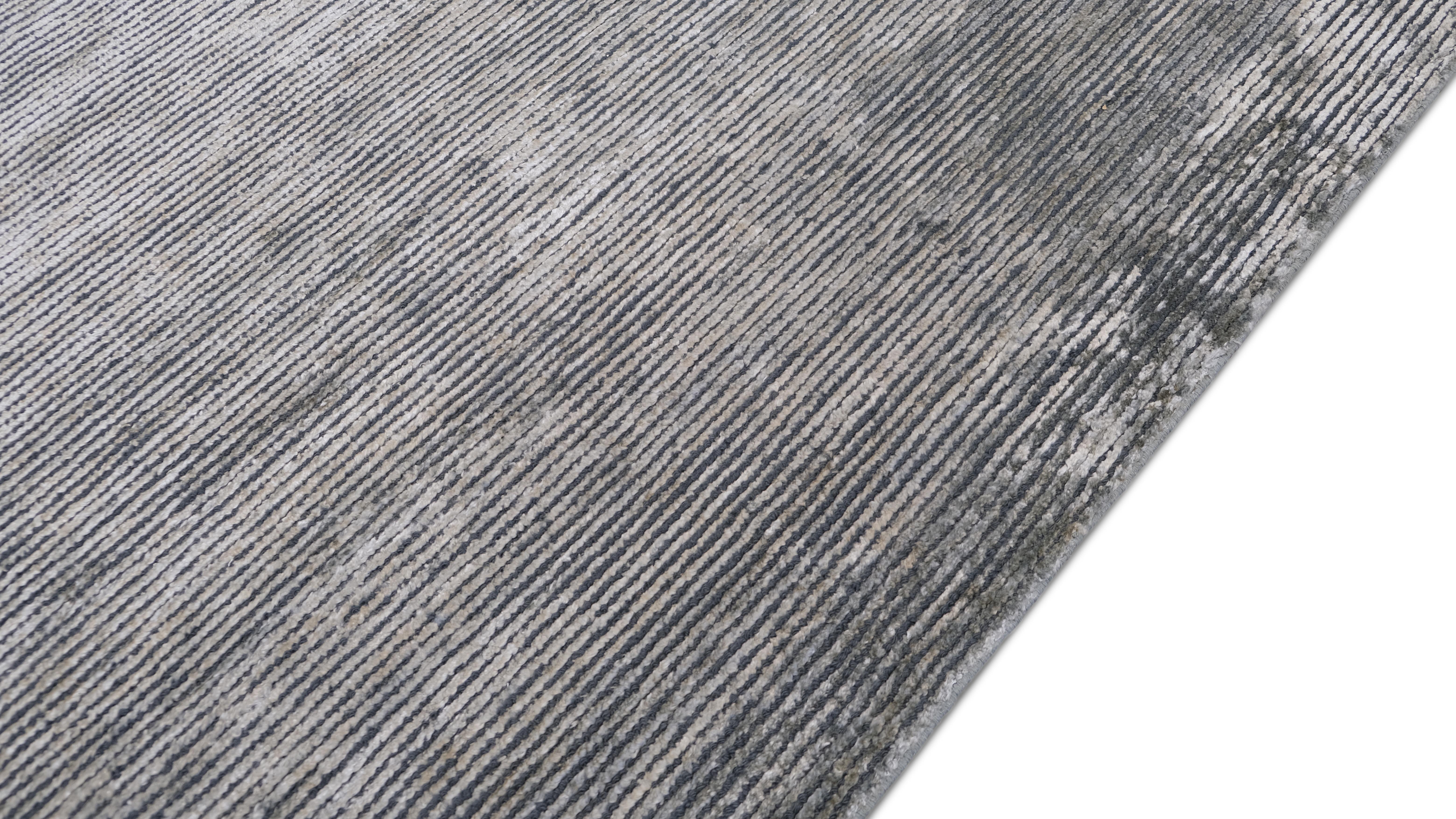 Eleganza sofisticata per questo tappeto in seta e lana di bambù annodato a mano. Caratterizzato da una sottile trama lineare a strisce nei toni del verde acqua, questo pezzo fonde il minimalismo moderno con l'artigianato di lusso, rendendolo una