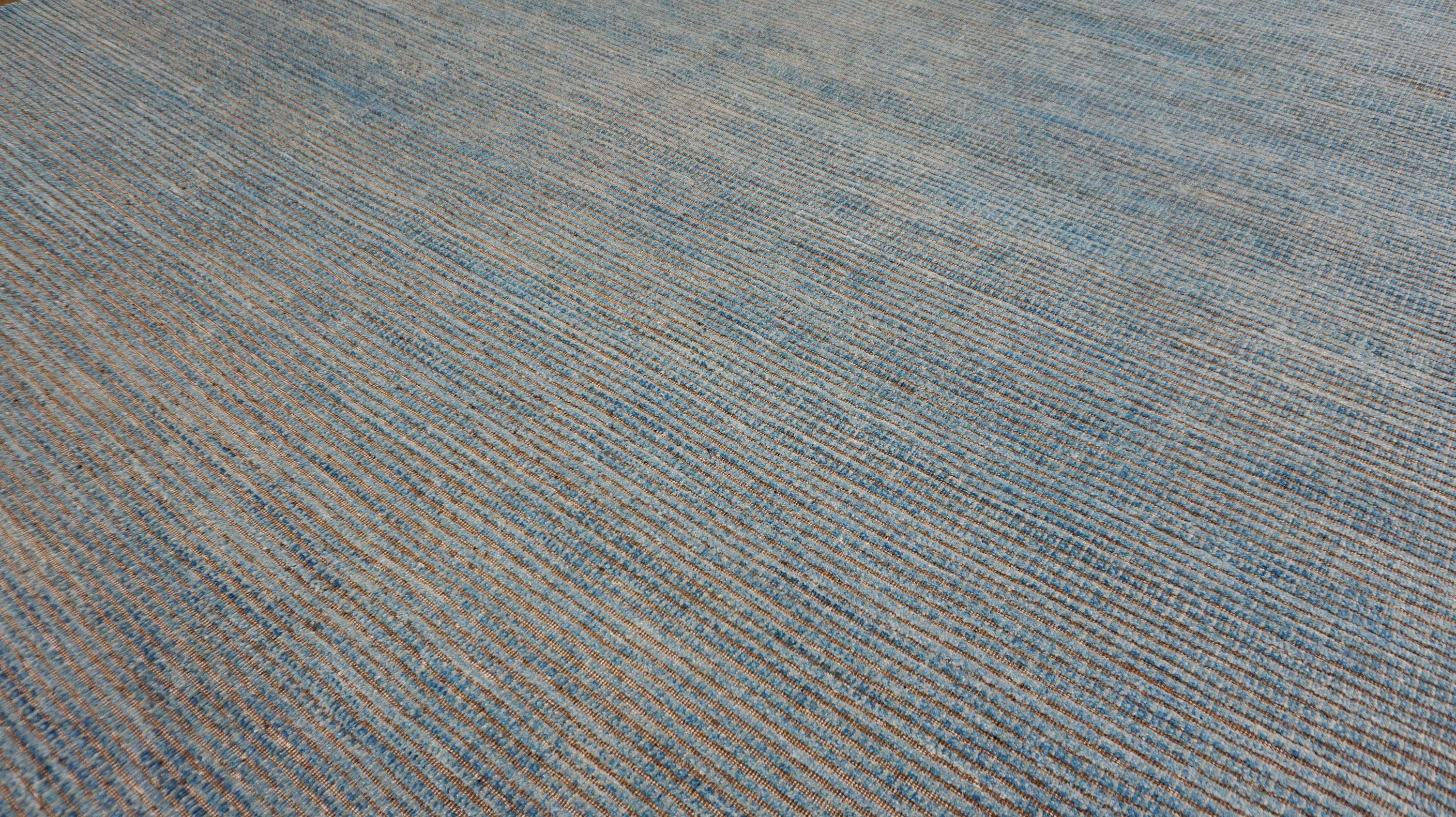This contemporary hand-knotted wool rug is a beautiful example of minimalist craftsmanship designed to complement modern and transitional interiors. Featuring a soft, serene palette of muted blue, tan  tones, the rug’s subtle abrash effect adds