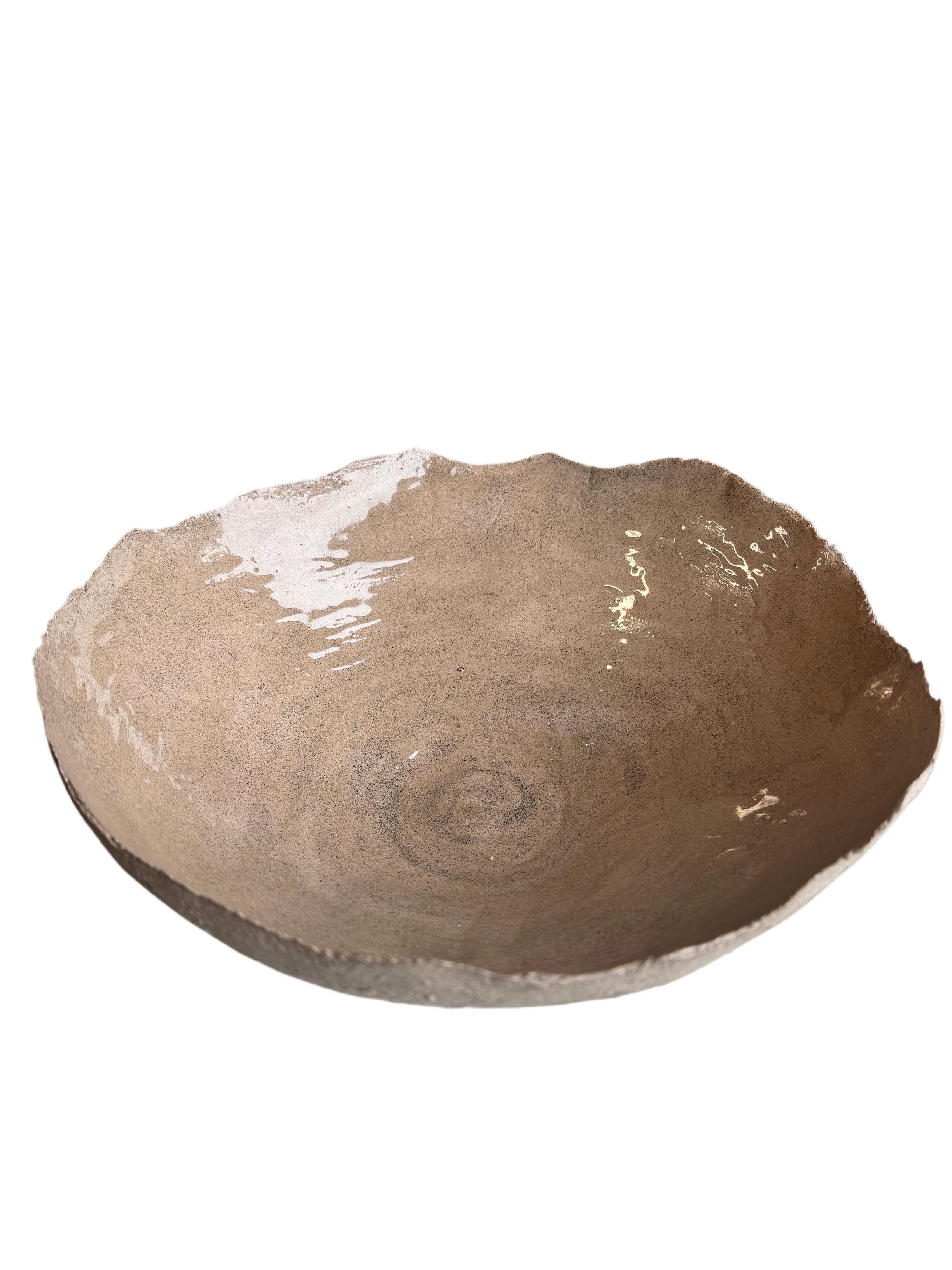 Este cuenco escultórico de cerámica, único en su especie, está hecho a mano en gres natural y acabado con un borde suavemente ondulado y un delicado esmalte interior. La textura de su superficie combina el tacto refinado con la crudeza de la tierra,