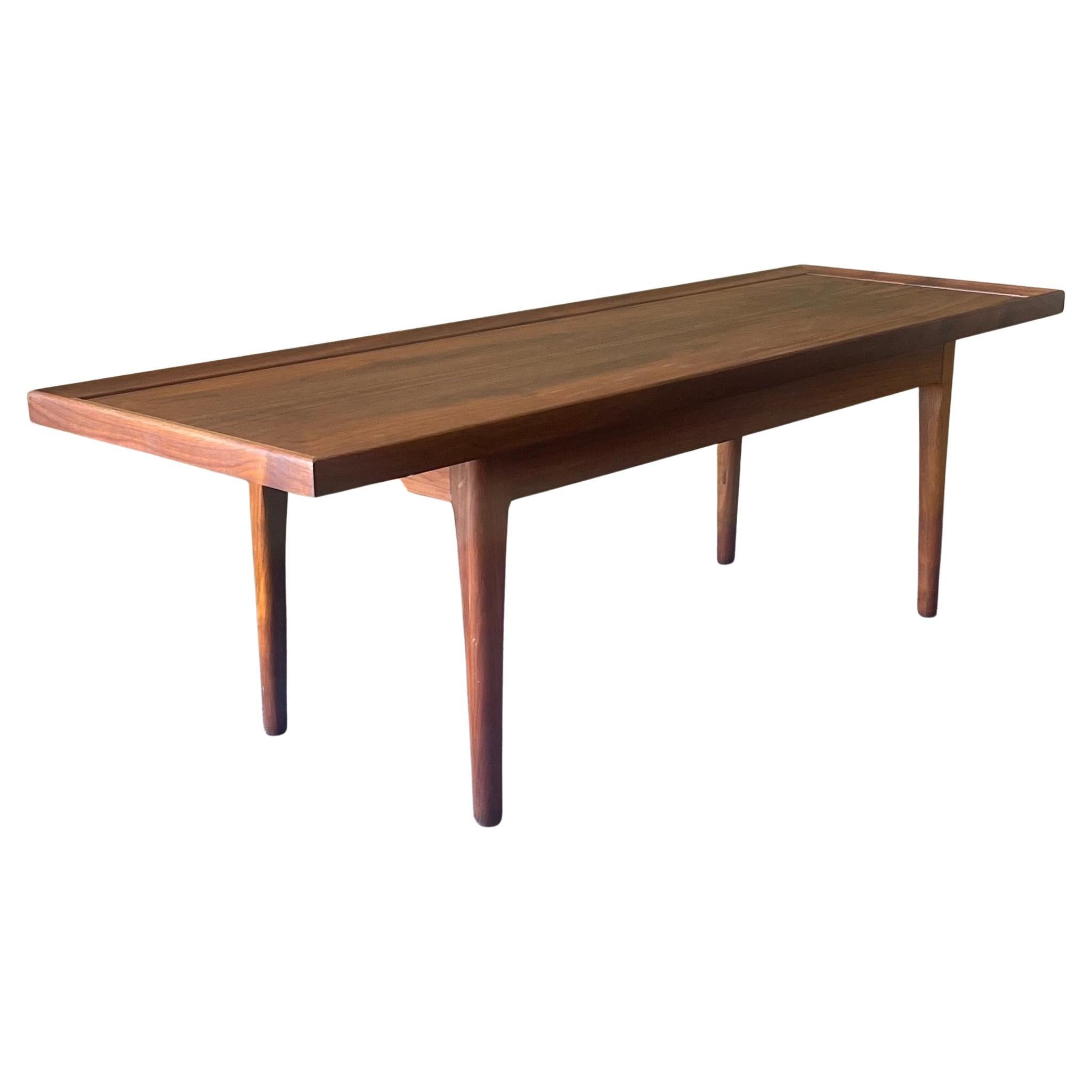 An exceptional minimalist low profile walnut coffee table by Kipp Stewart for Drexel - Declaration line, circa 1960s. The table has both a gorgeous tone and grain which is contrasted by an ebony inlay detail running along the tabletop near the