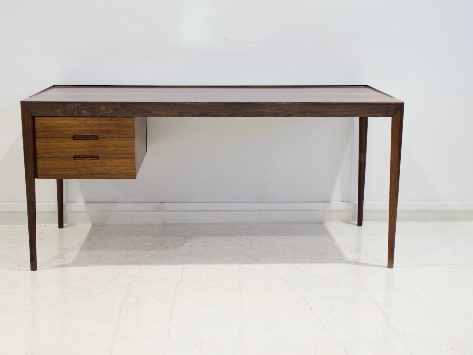 Sleek desk made of hardwood with partly raised edge. Slim tapered legs. Drawer section with three drawers. Designed by Erik Riisager Hansen and manufactured by Haslev Møbelsnedkeri.
Literature: Catalogue from Danish Furniture Maker's Control