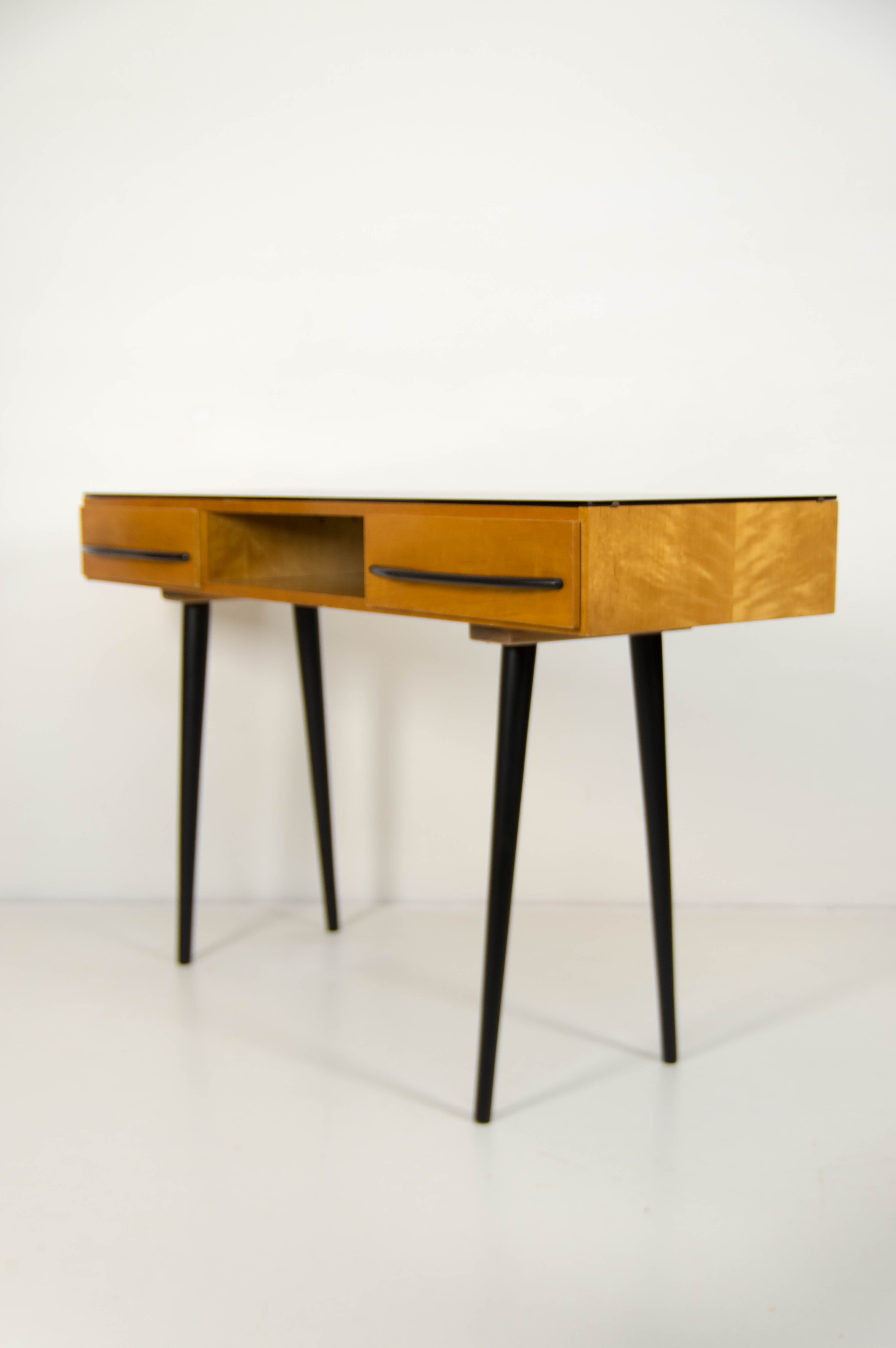 Exceptional mid-century writing desk designed by Mojmír Požár and produced by UP Závody in Czechoslovakia in the 1960s. The desk features elegant, tapered black legs, two spacious drawers, and a preserved veneered body with new black glass top. Its