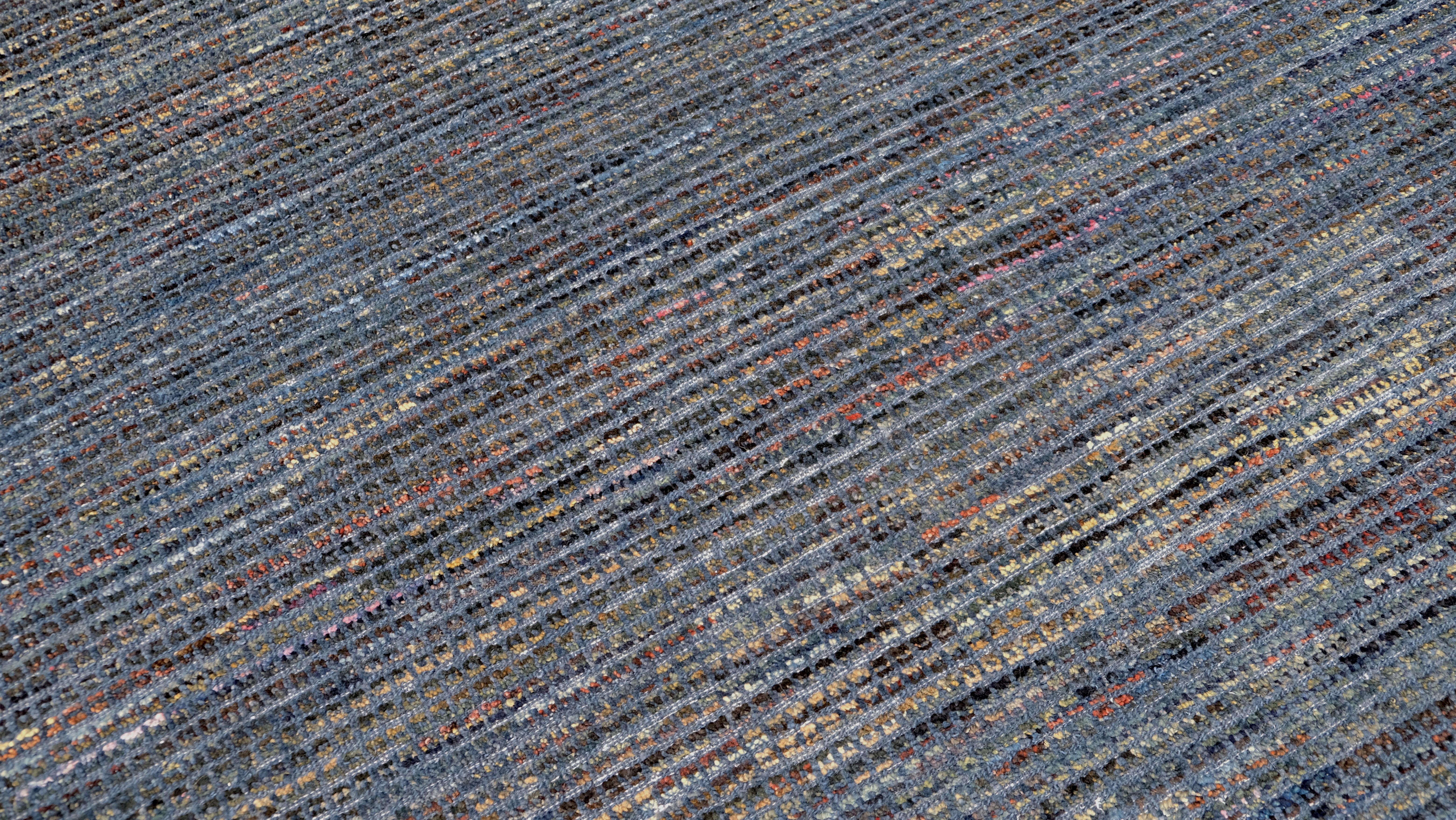 Dieser handgeknüpfte Wollteppich zeigt ein reich strukturiertes Streifenmuster in einer raffinierten Palette von tiefen und gedämpften Blautönen mit subtilen Tonalvariationen. Die aufwendige Webtechnik sorgt für eine moderne und doch zeitlose