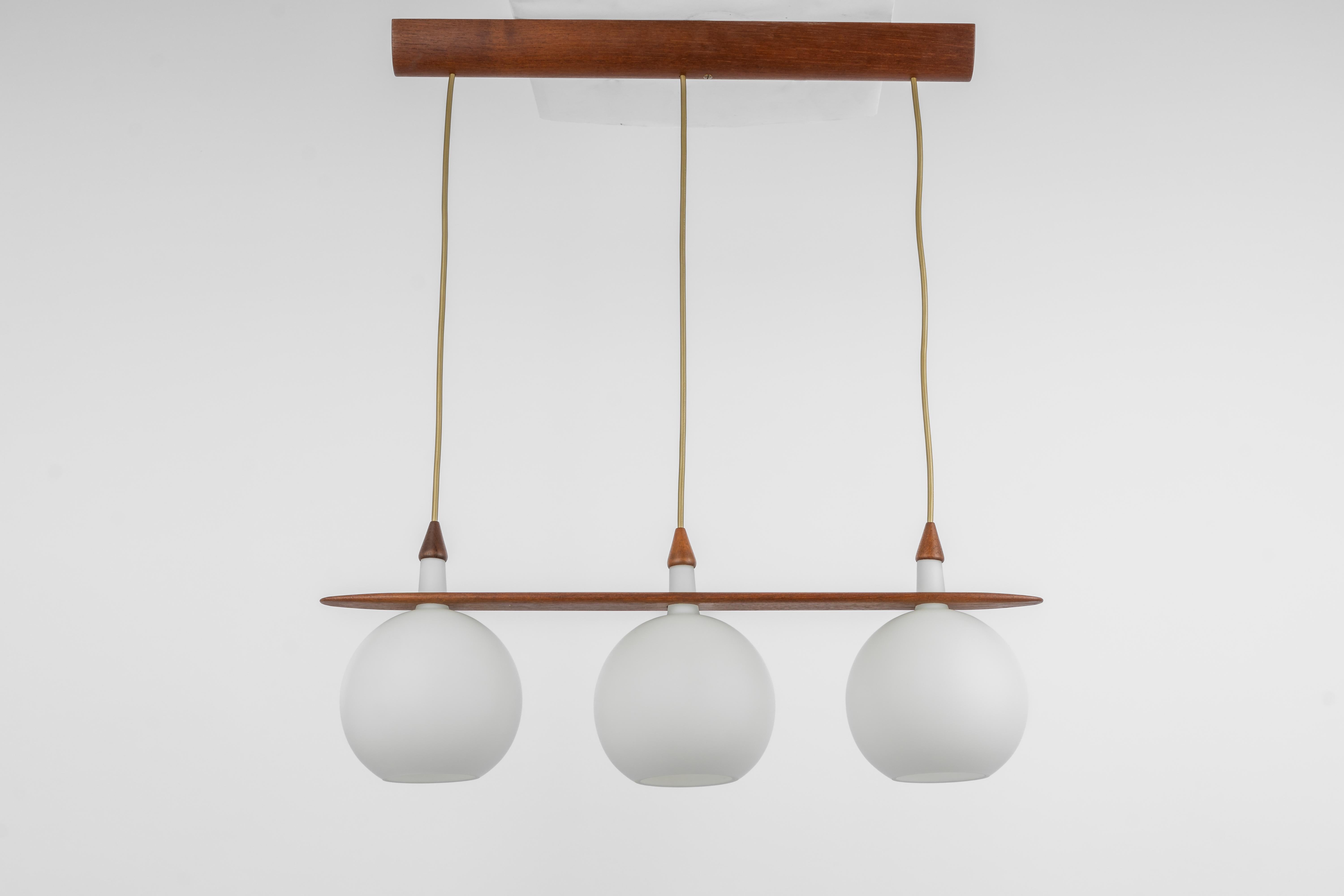 A wonderful midcentury teak chandelier. A unique, timeless, and elegant masterpiece of Danish Teak wood designed by Uno & Östen Kristiansson, Sweden, 1960s. The light sculpture impresses with the perfect materials of wood and opal glass. 

High