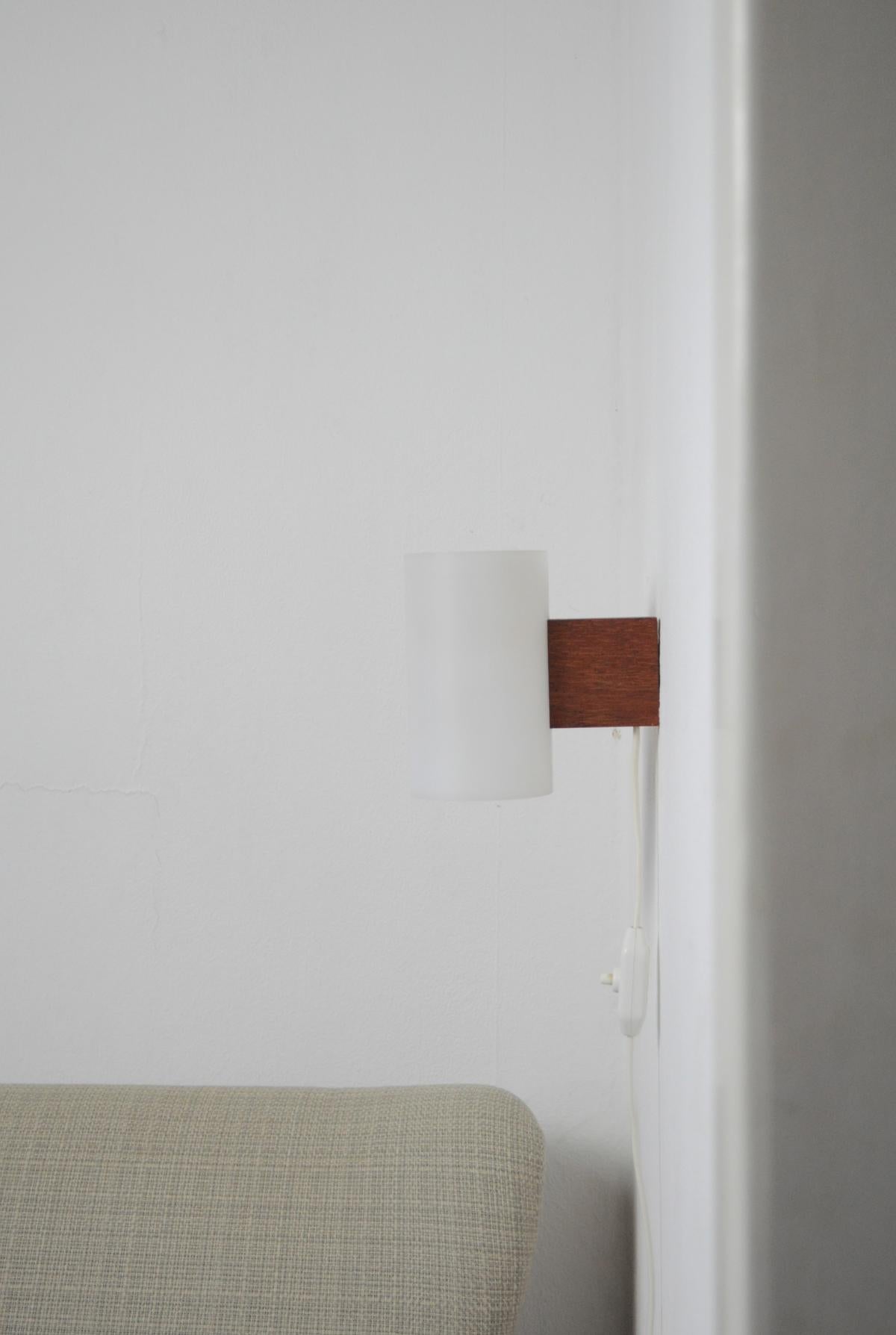 Swedish teak and acrylate wall lamp designed by Uno & Östen Kristiansson and manufactured by Luxus, Sweden. 
Magnificent minimalistic design.

Diameter of lamp shade: 8 cm 
Height: 13.5 cm
Depth: 13.5 cm