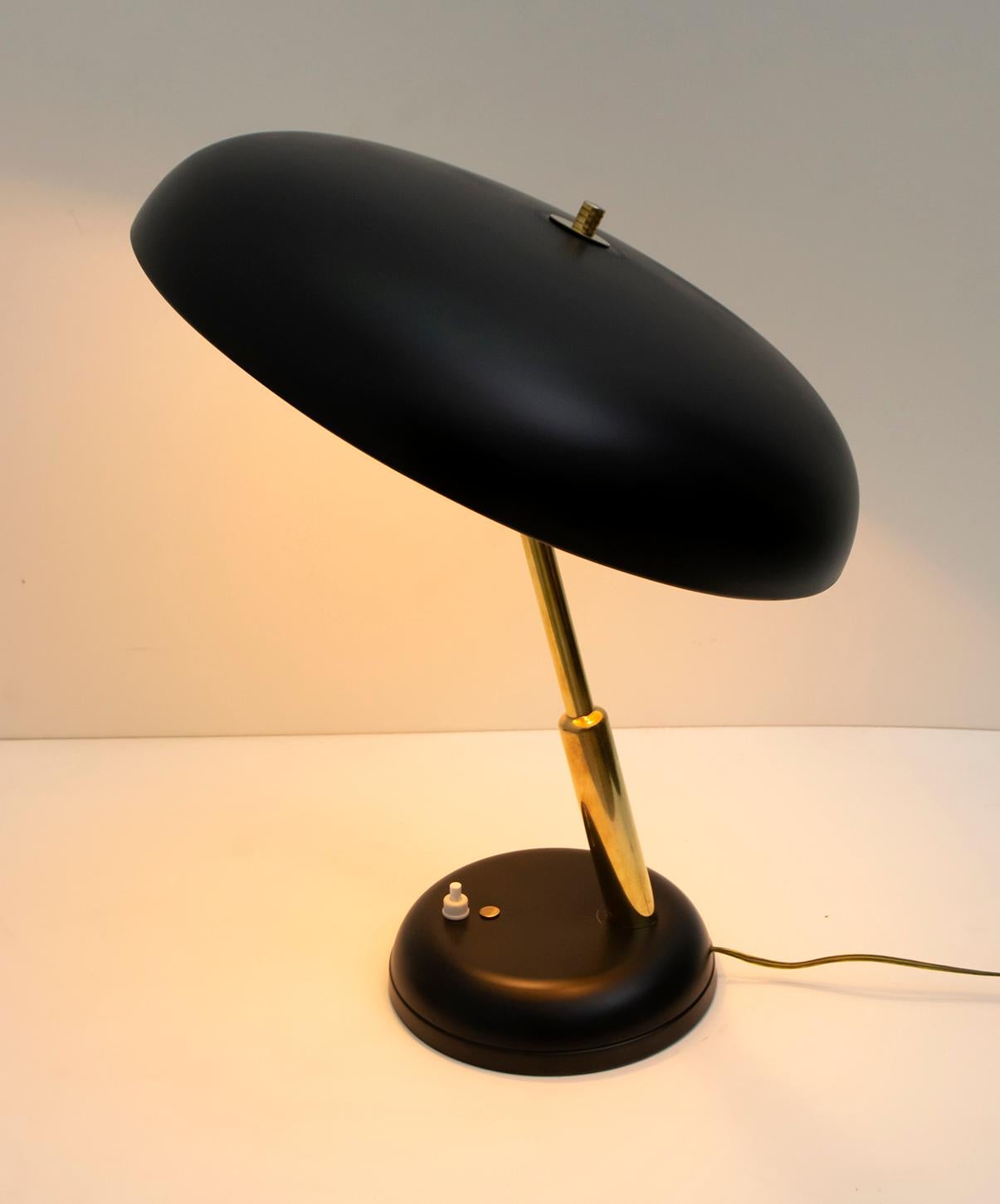 Elegant ministerial lamp made of brass and black lacquered aluminum, 1950s. The round base with beveled edge has a diameter of Ø17 cm, a mushroom-shaped hat of Ø30 cm, in black lacquered aluminum, the stem in brass. Height 40 cm. The antique