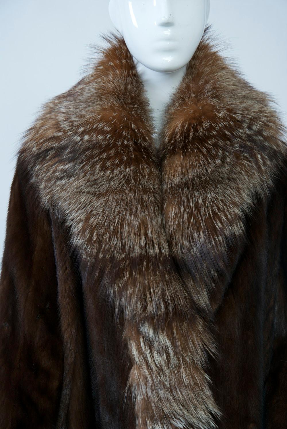 Eye-catching mahogany mink coat featuring fox trim around all edges and cuffs. Lustrous vertical mink skins with side pockets. Can be buttoned up at neck for extra warmth. Fur clasps in front. Animal print and floral lining. Labelled 