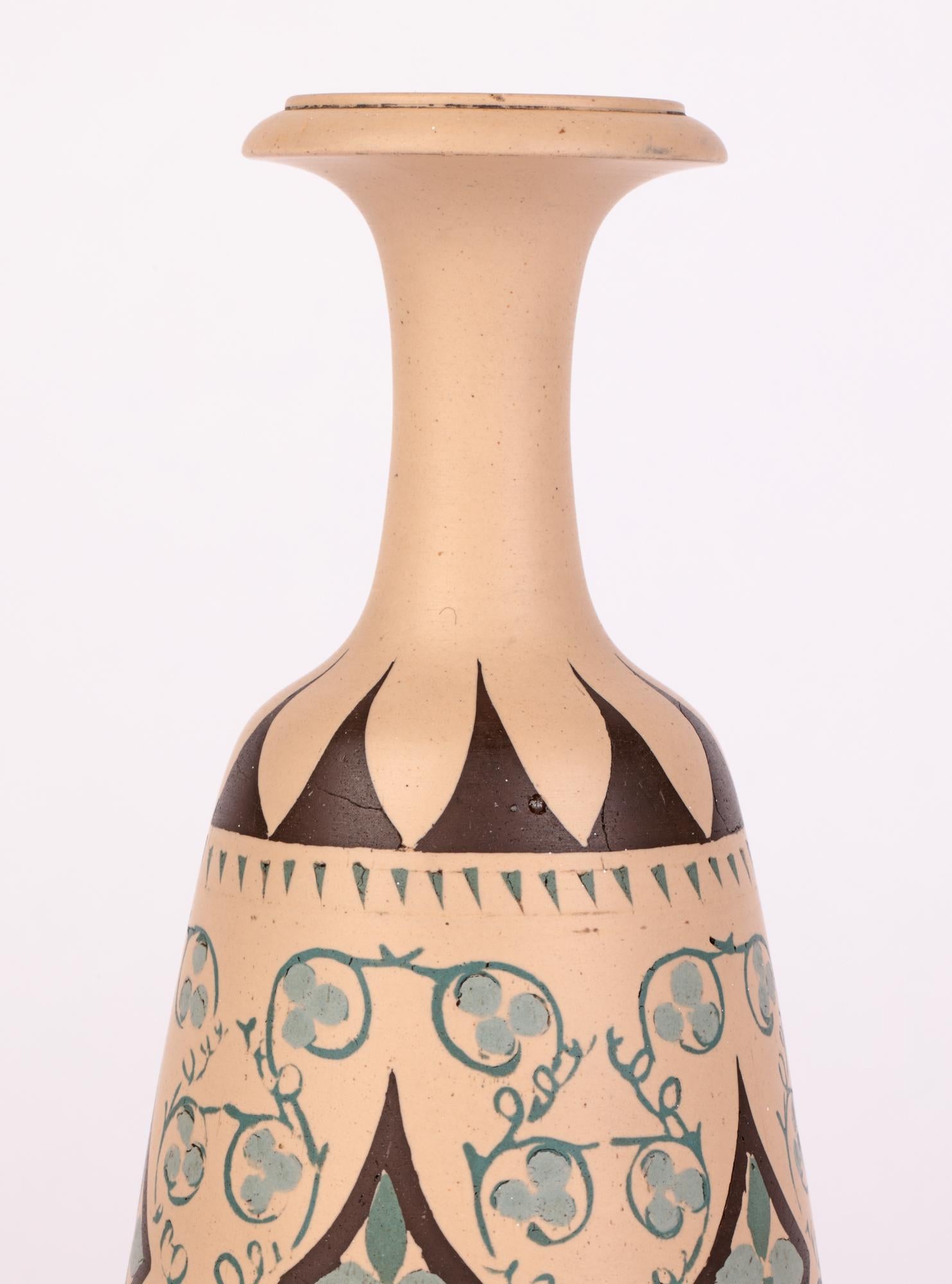 A very unusual Aesthetic Movement biscuit fired Doulton Lambeth stoneware vase pigment hand-painted with stylized foliage and geometric designs by Minnie G Thompson and dated 1883. The tall vase stands on a wide round pedestal foot with a tapering