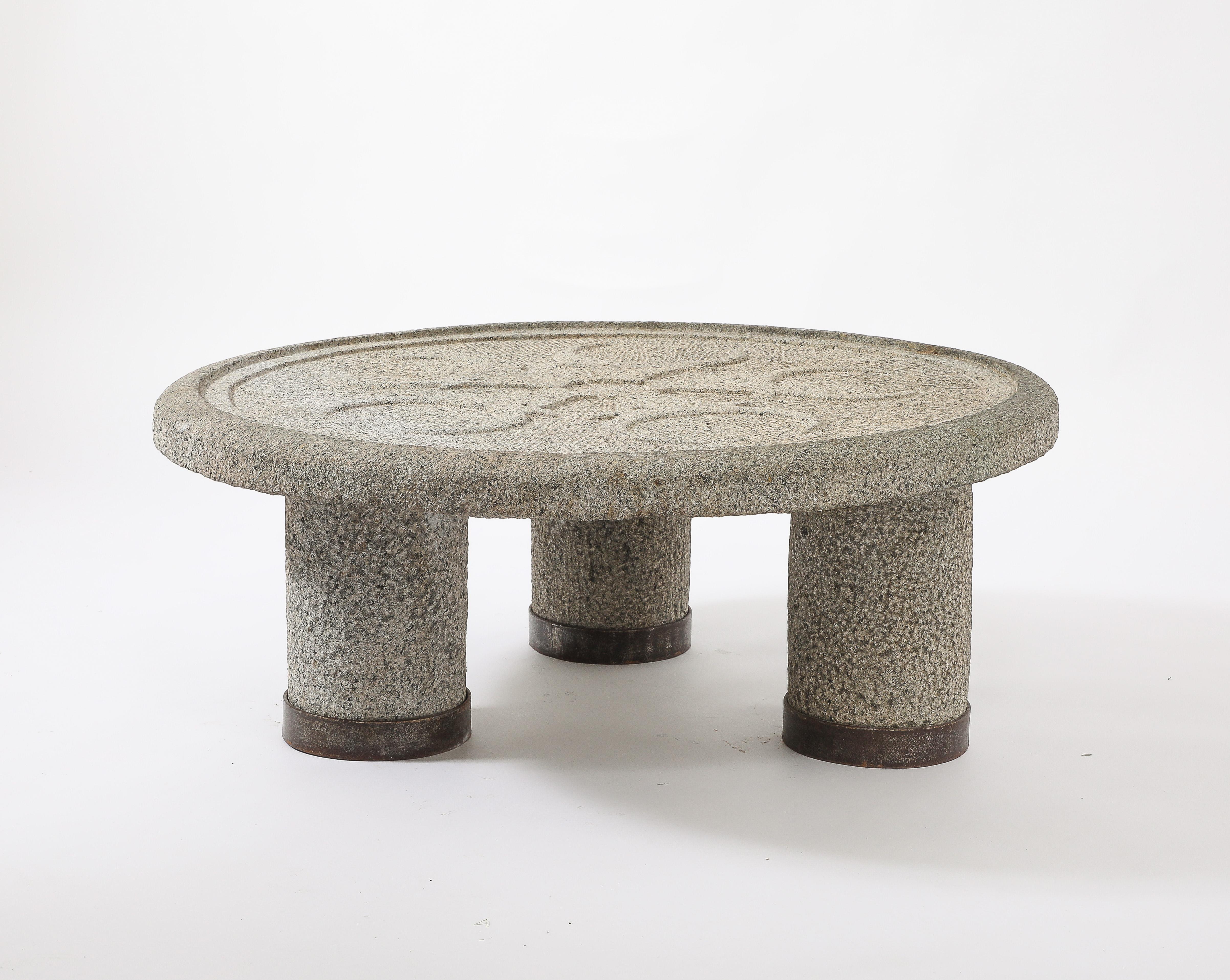 Exceptionnelle table basse en pierre massive sculptée, le plateau est une pierre unique de 35'' de diamètre par 5'' d'épaisseur avec un motif sculpté en creux de 5 têtes de minotaures, elle repose sur des pieds en pierre tout aussi massifs, terminés