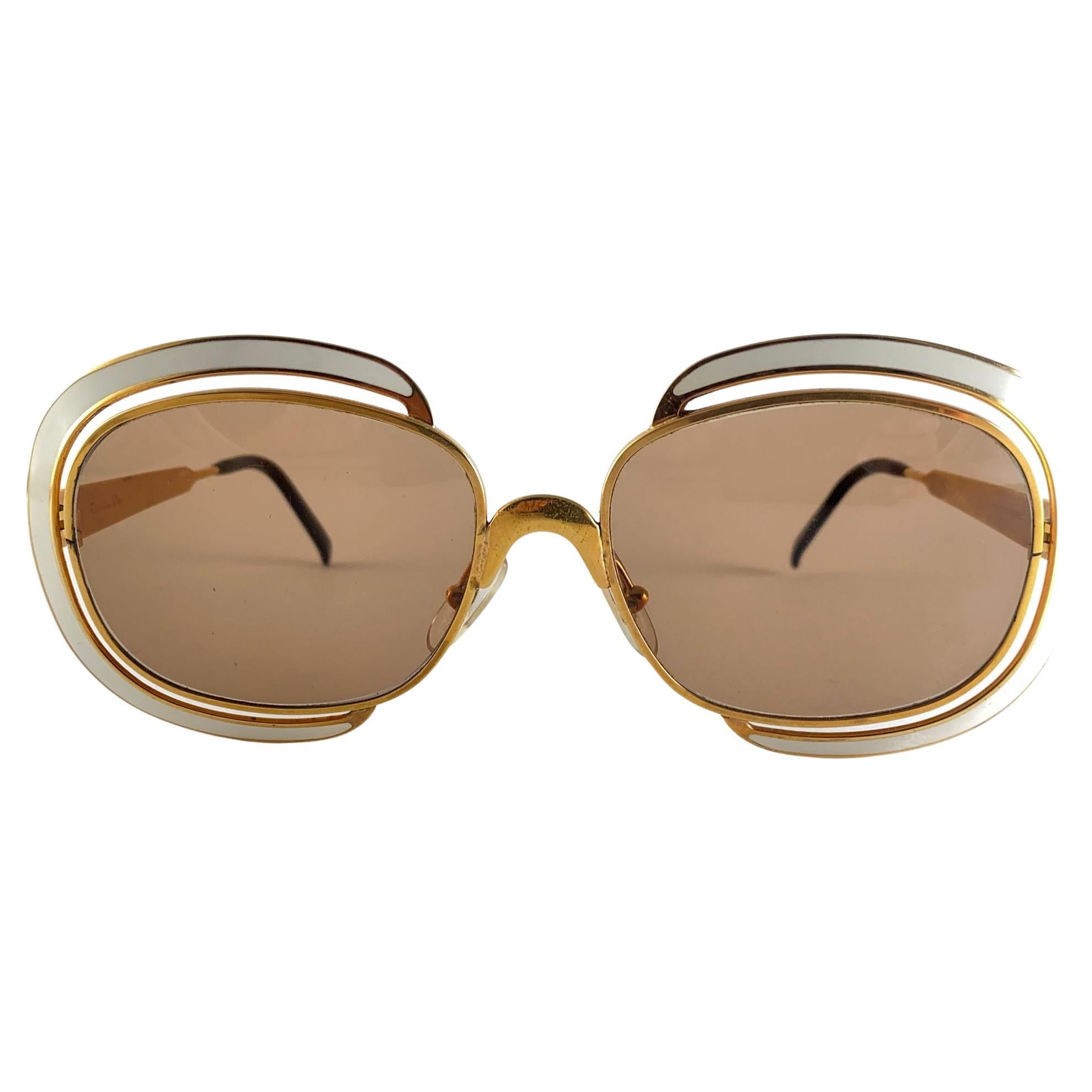 Mint Vintage Christian Dior Sunglasses. 
Beige Enamel Details Over A Gold Frame.

Light Brown Lenses Lenses.

The Enamel Coating Is Missing A Piece On The Left Temple.

Made In Austria

Front  14 Cms
Lens Height 4.3 Cms
Lens Width 5.3 Cms
Temples