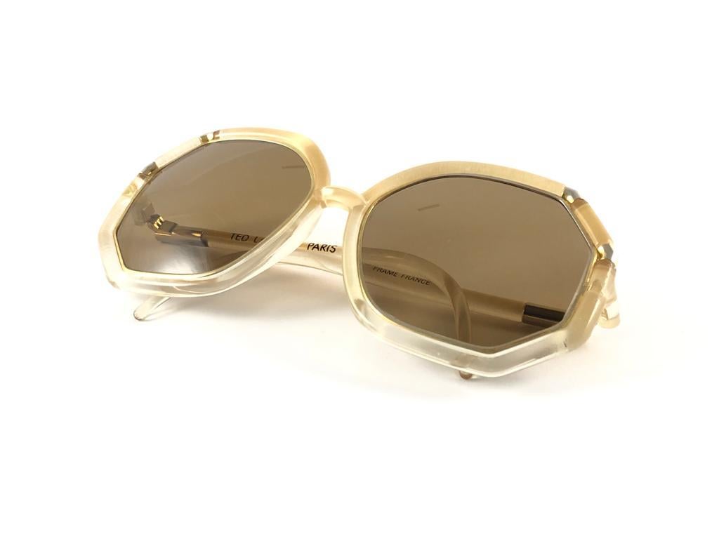 Mint Vintage Ted Lapidus Beige & gold frame with spotless medium brown lenses.  
Made in Paris.  
Produced and design in 1970's.  
This item have minor sign of wear on the frame. Please study the pictures prior purchase.

FRONT 14.5 CMS
LENS HEIGHT