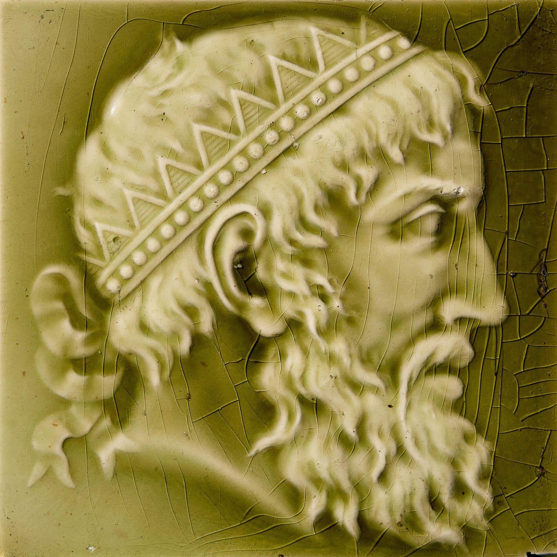 Un ancien carreau de faïence vert olive de 6 pouces de Minton & Co. (estampillé) représentant un portrait de profil d'un personnage néoclassique barbu portant une coiffe royale. Autrefois utilisé pour décorer une cheminée, ce carreau original de